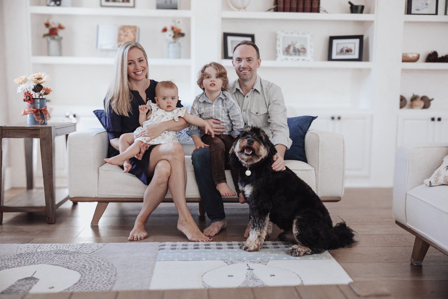 Two dogs and their family relax together on a light colored couch in a cozy modern living room.