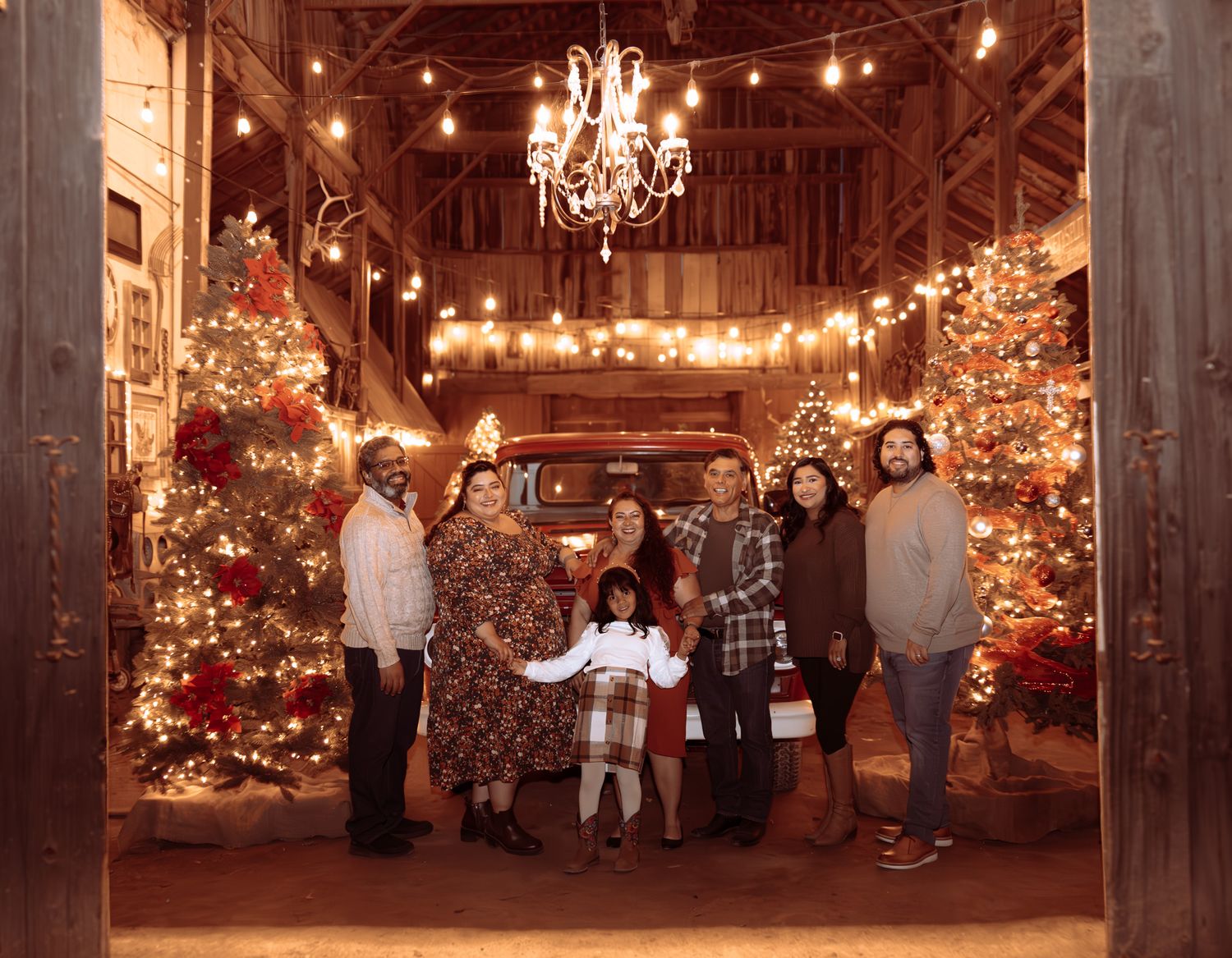 A rustic barn interior decorated with twinkling string lights and Christmas trees creates a warm, festive atmosphere.