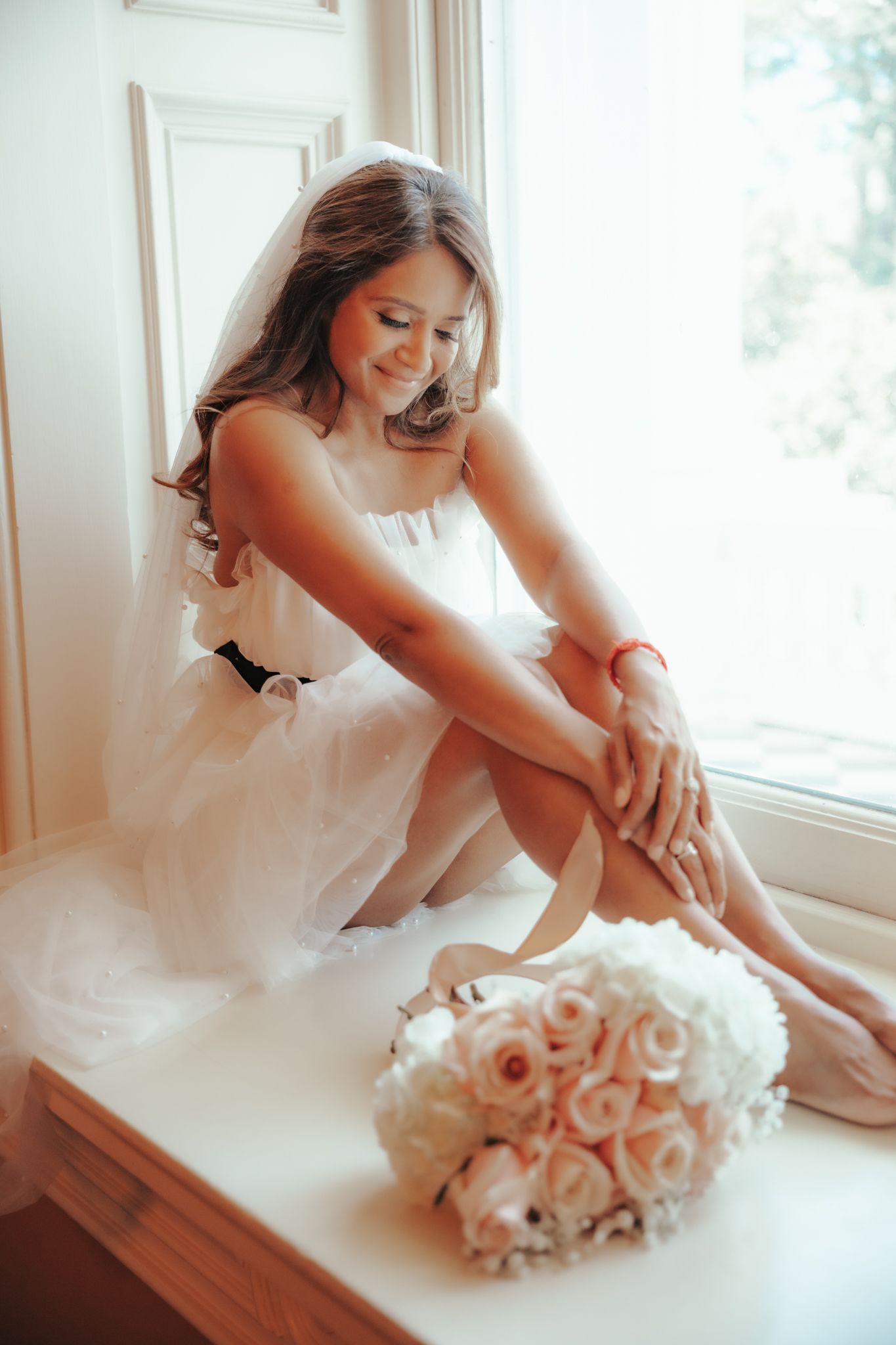 A romantic bridal portrait series shows delicate moments with light pink roses by a sunlit window.