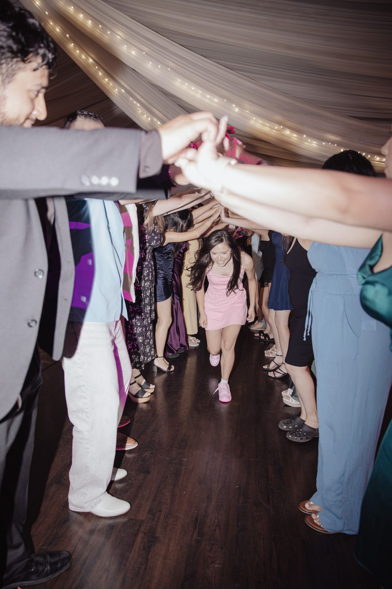 Quinceañera walking through a hands‑in‑hand arch on the dance floor at her Oakland, CA celebration.