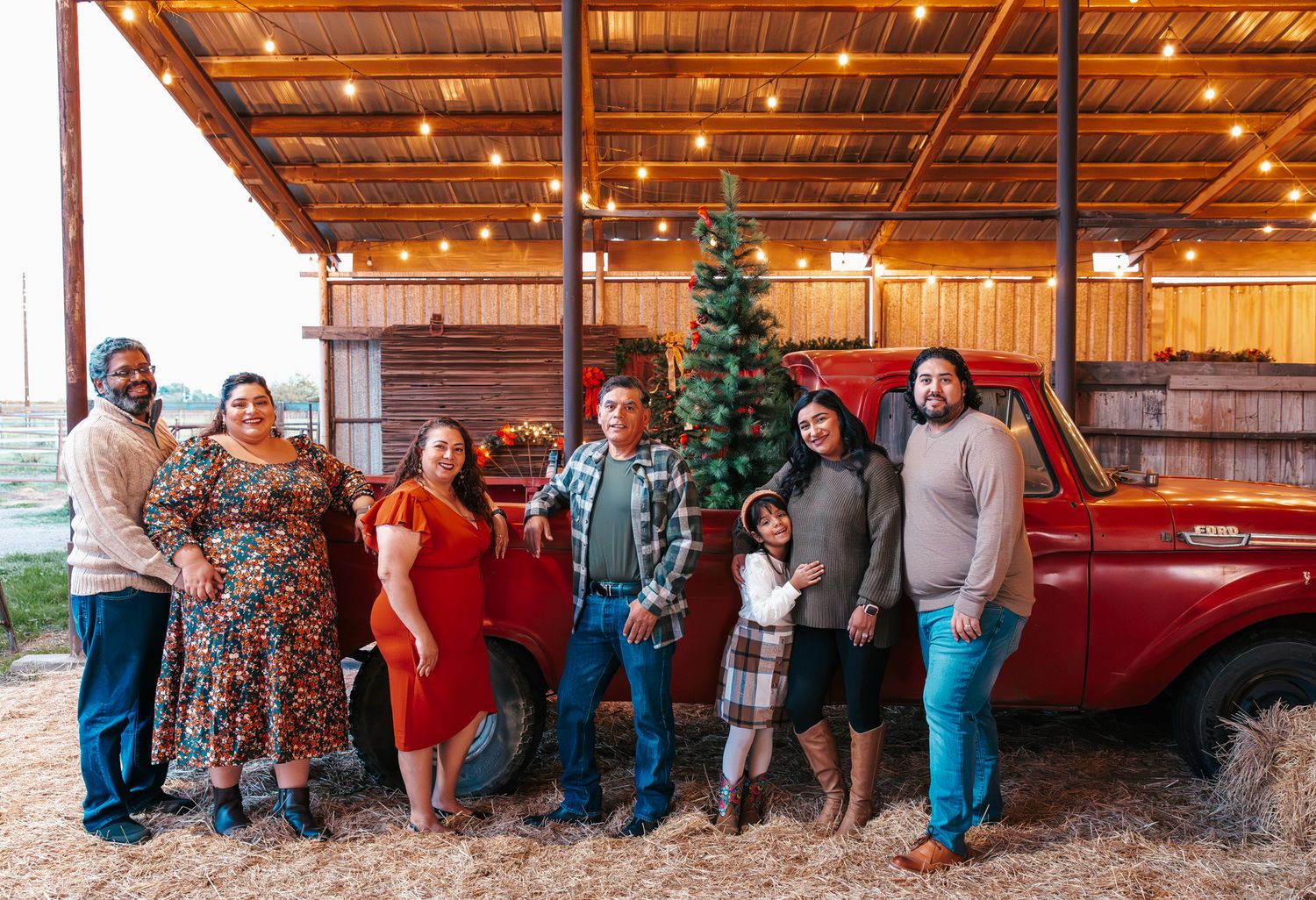 A group of people pose together in front of a rustic wooden barn with warm lighting and holiday decorations.