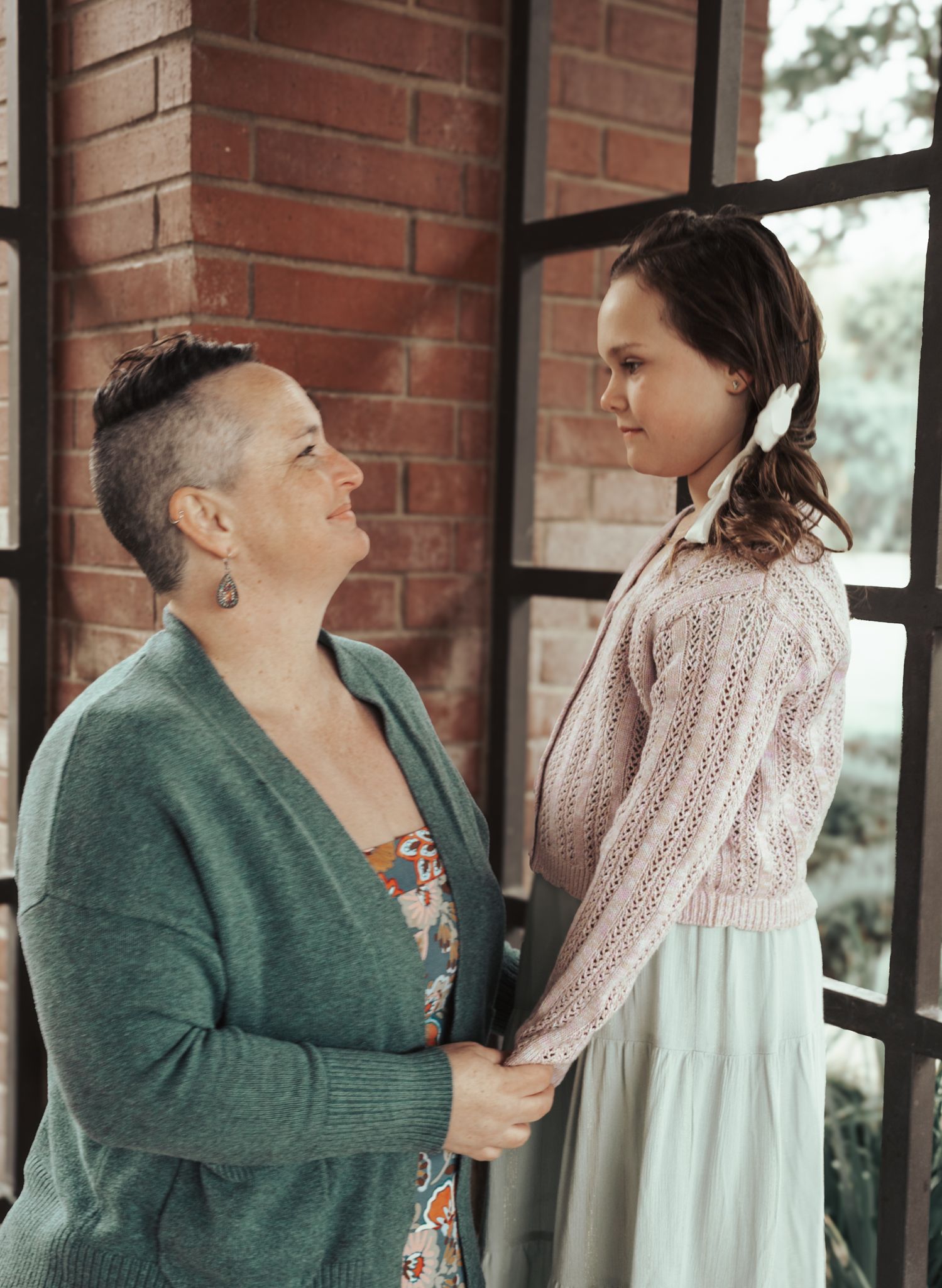 A heartfelt moment between two people wearing cozy sweaters standing in front of a brick wall near a window.