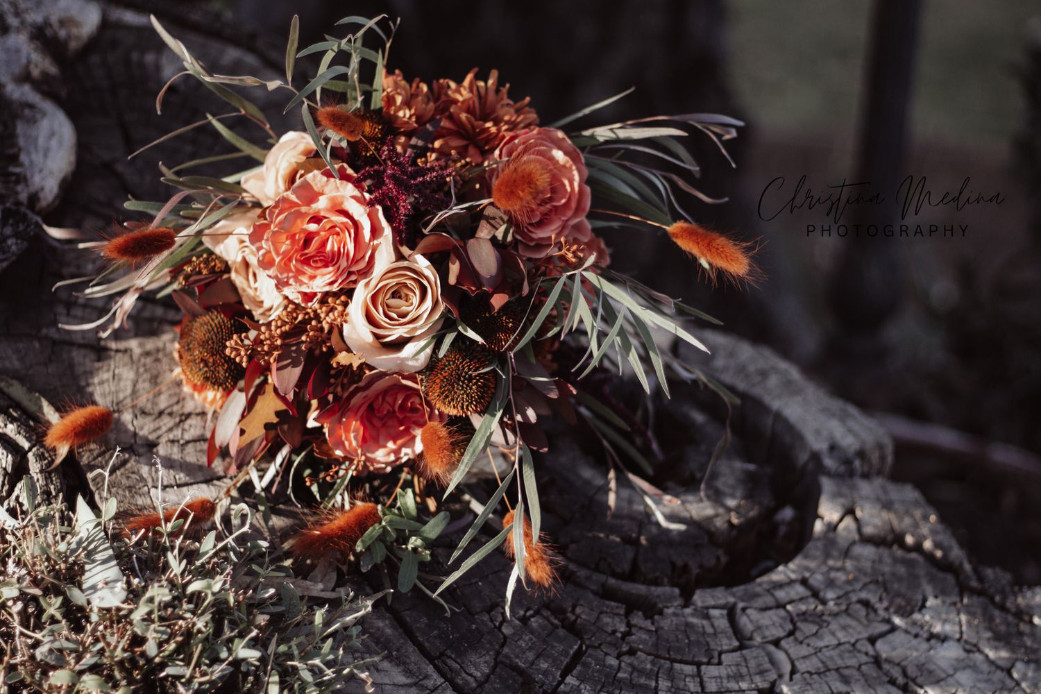 Dark and moody floral arrangement with dried roses and autumn foliage against a textured stone background.