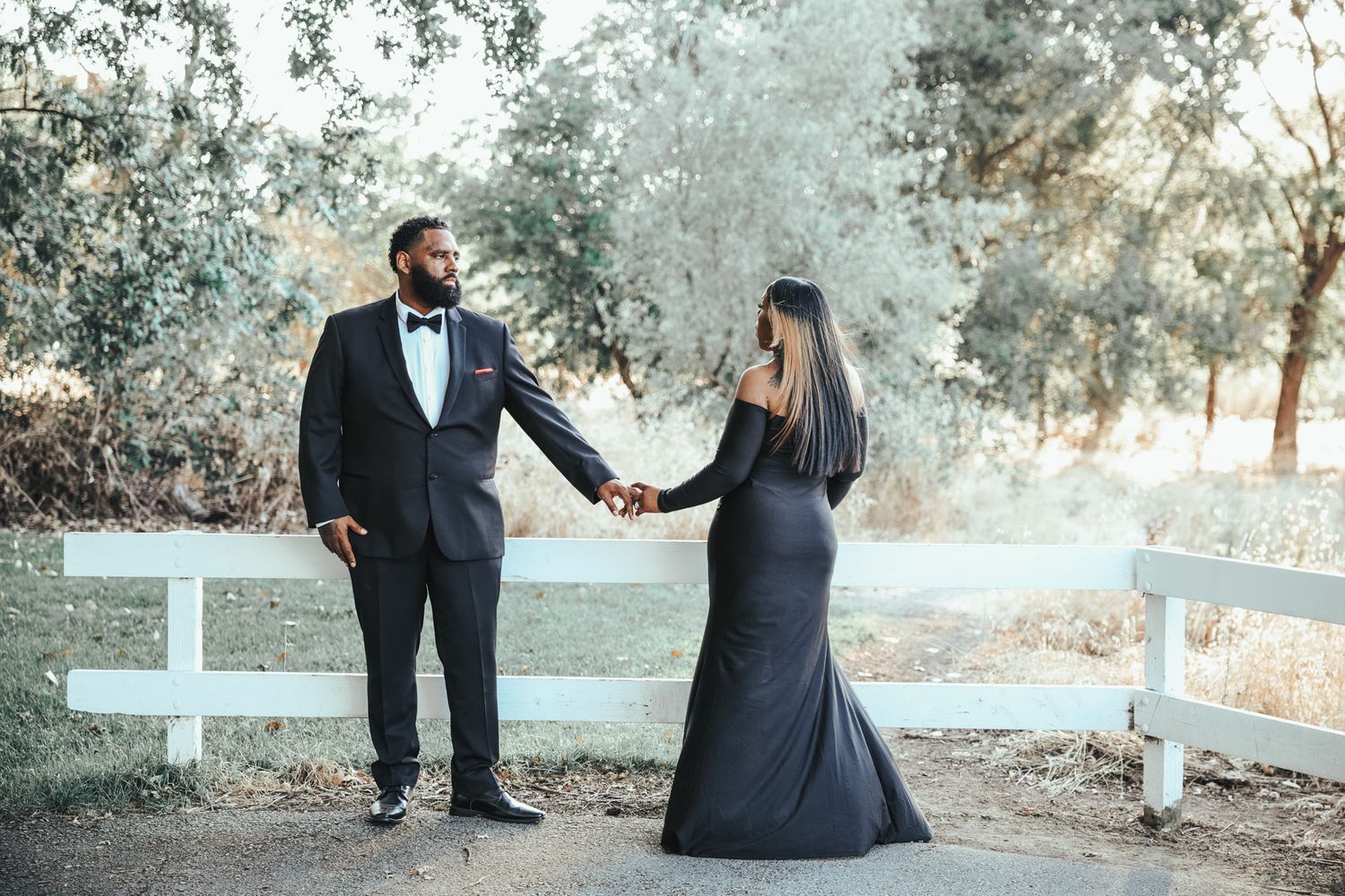 A couple in formal attire poses together in a dreamy outdoor setting with white crosses visible in the background.