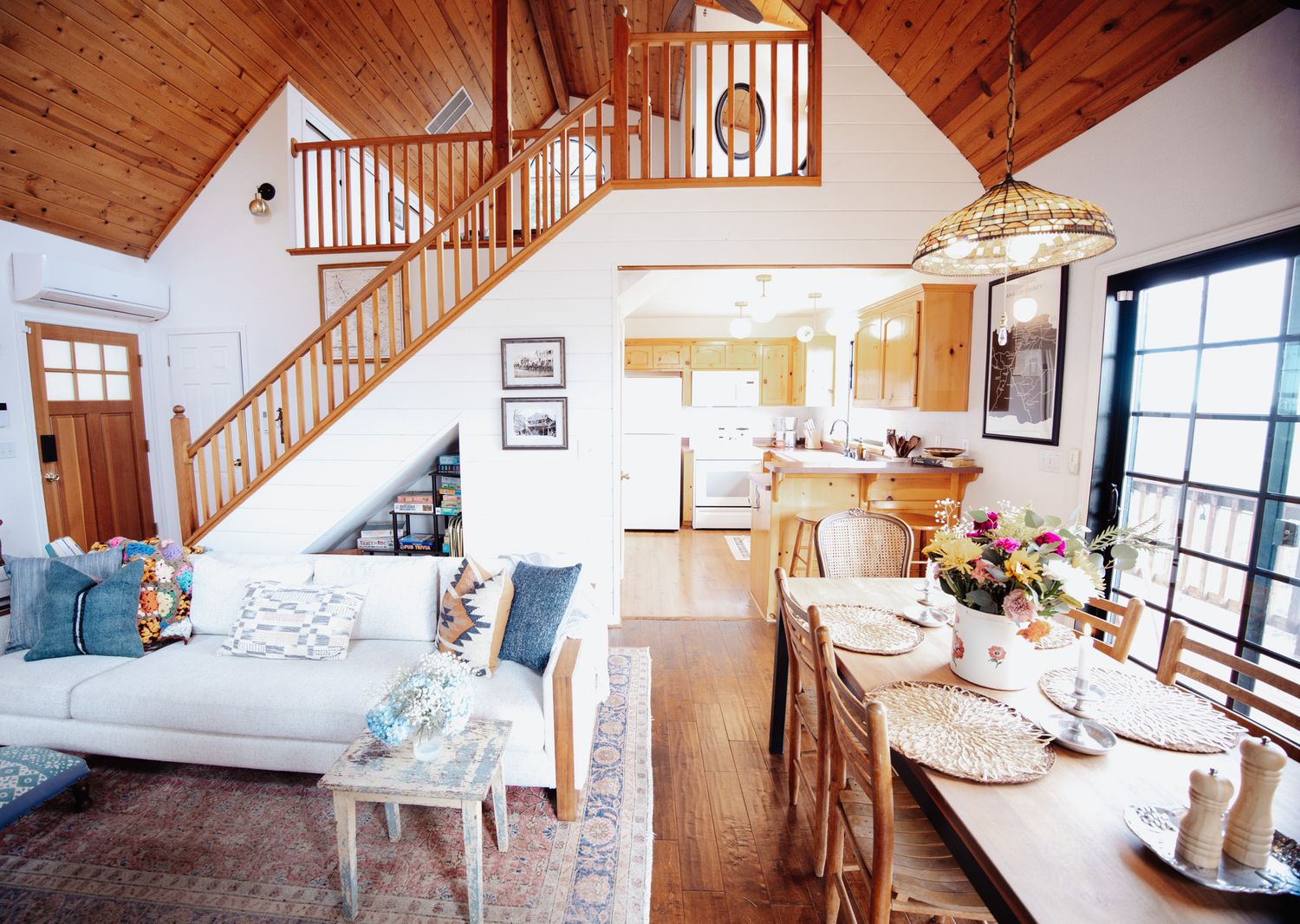 A modern cabin interior with wood paneled ceilings and stairs features an open concept design and coastal decor elements.