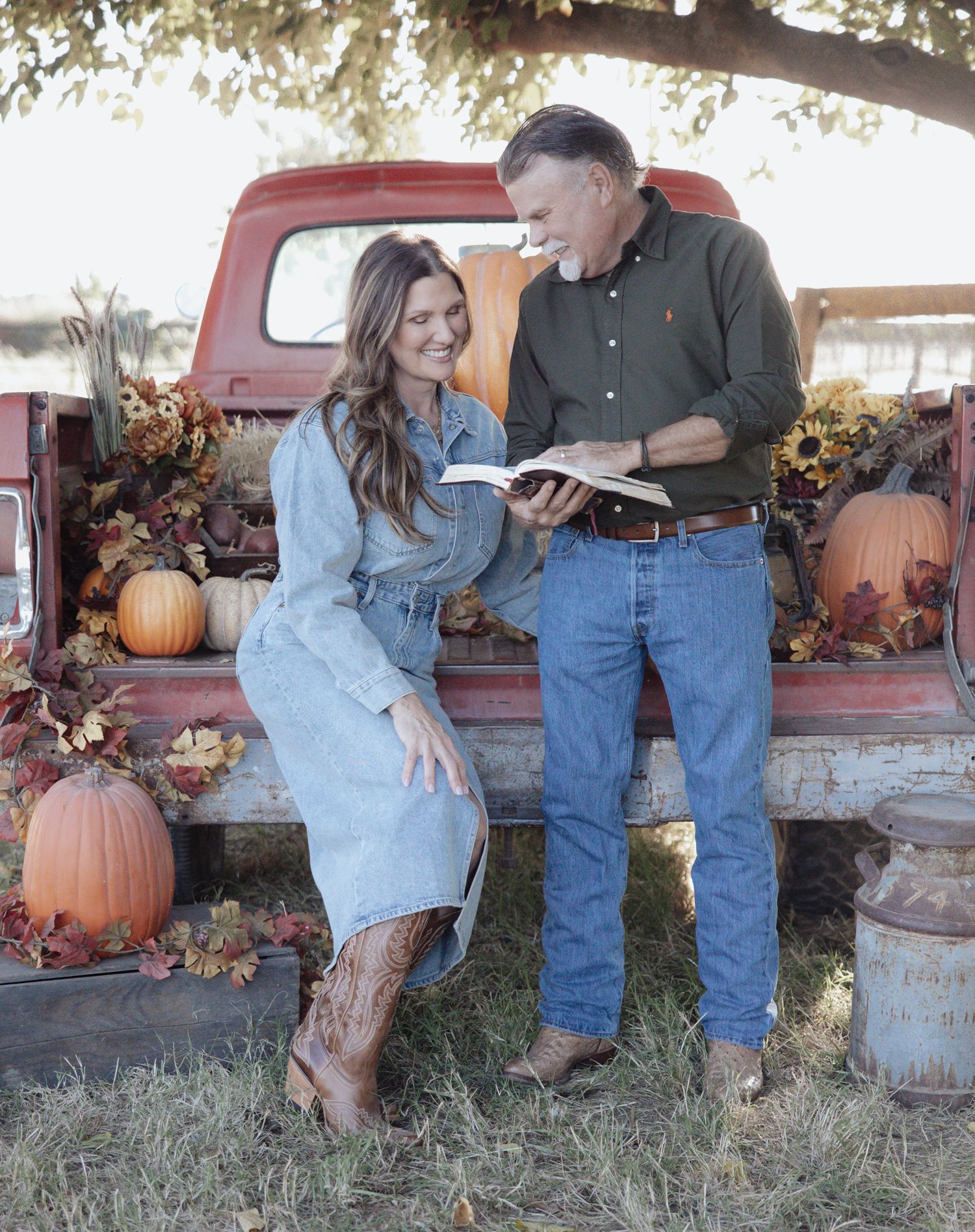 A couple poses together at a rustic autumn pumpkin patch with vintage red trucks and fall decor in the background.