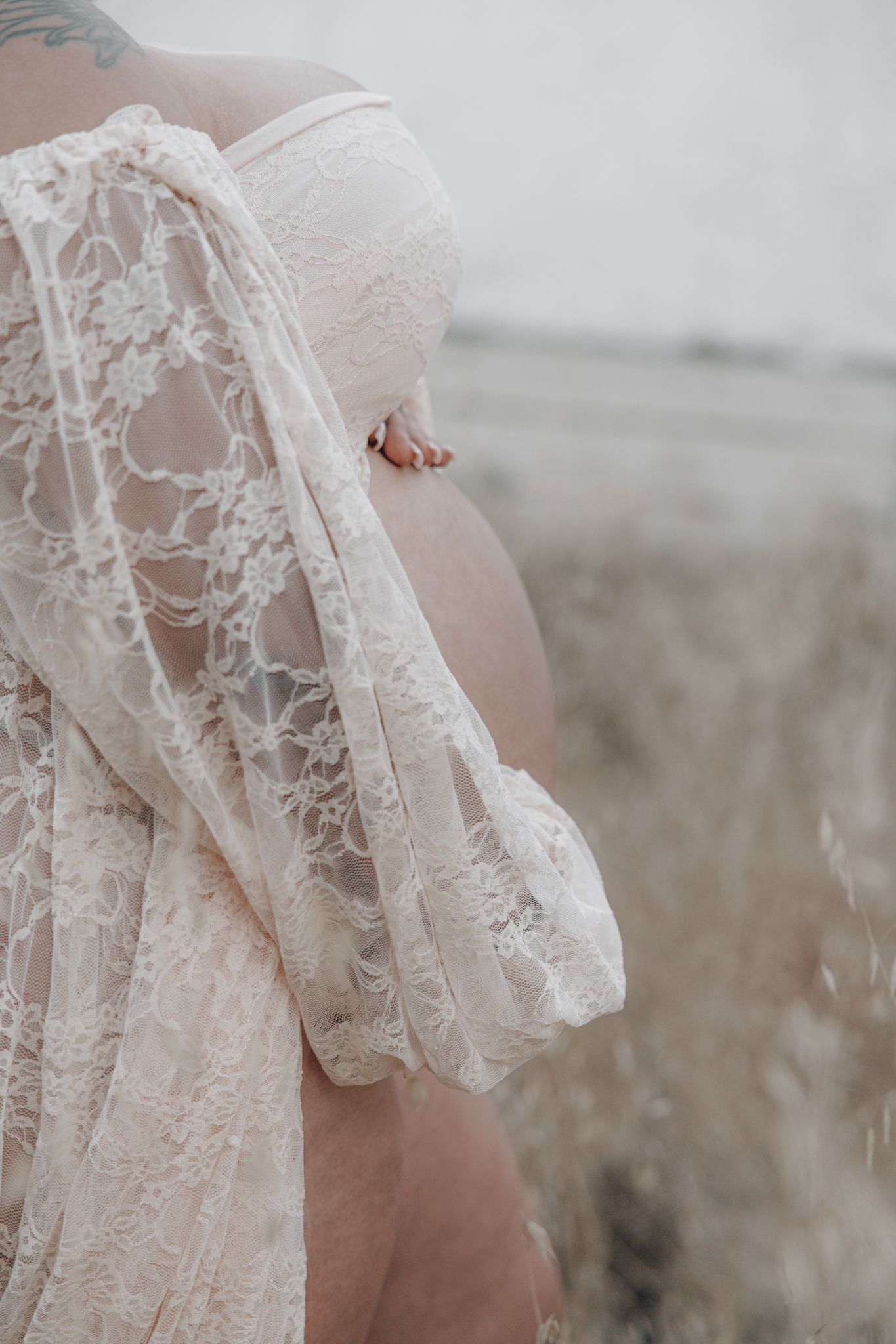 A delicate white lace maternity dress with flowing sleeves photographed against a soft outdoor background.