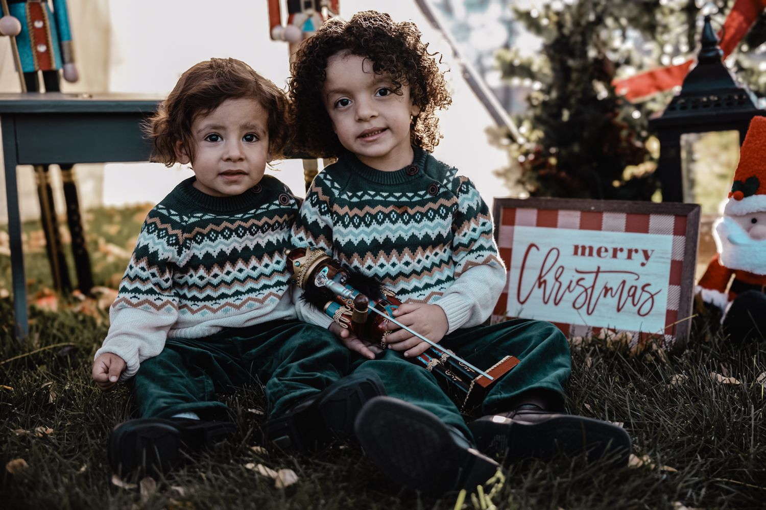 Two young children sit together outdoors wearing matching sweaters with geometric patterns during winter.