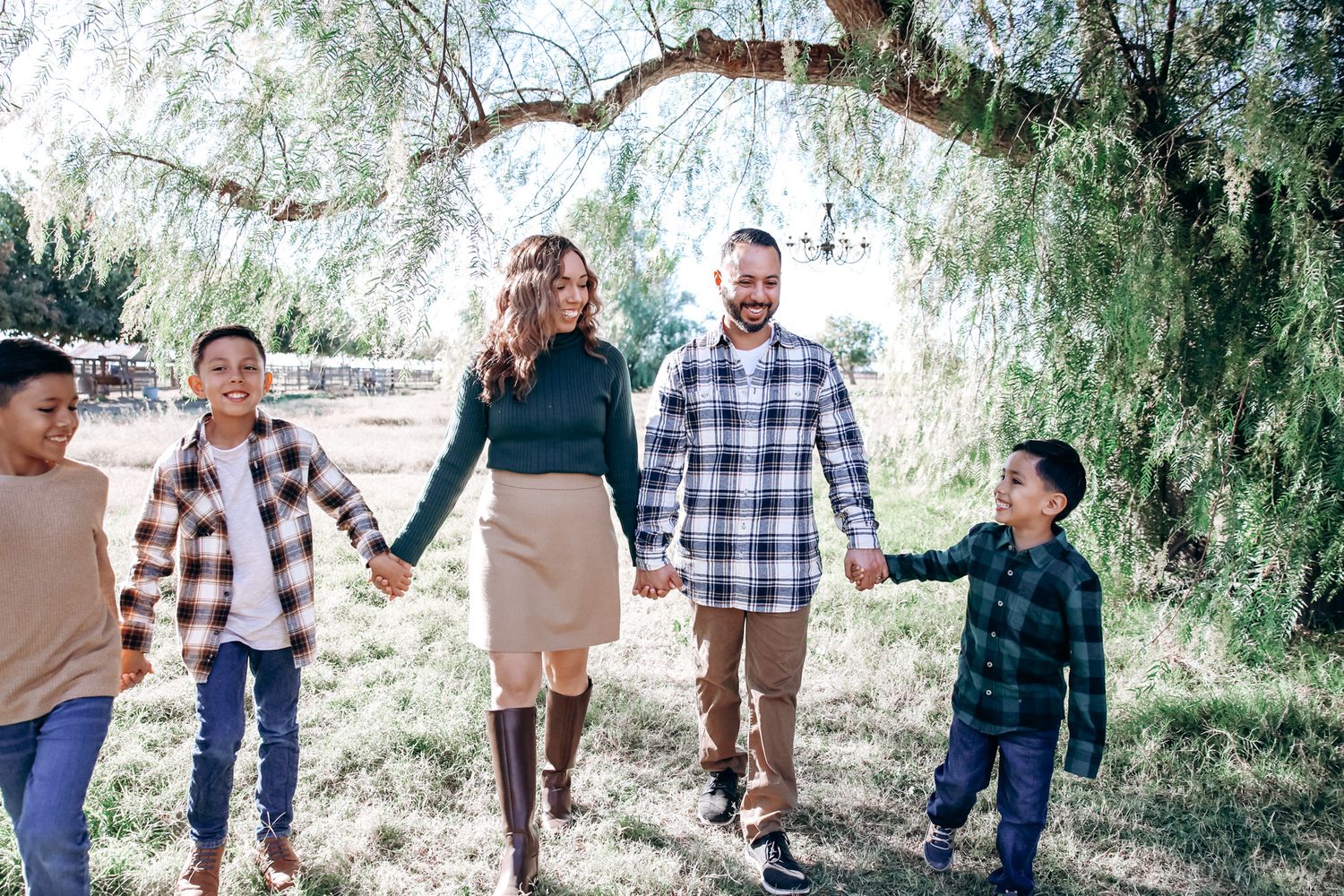 Family members walk together on a tree-lined path on a sunny afternoon wearing coordinated casual outfits.