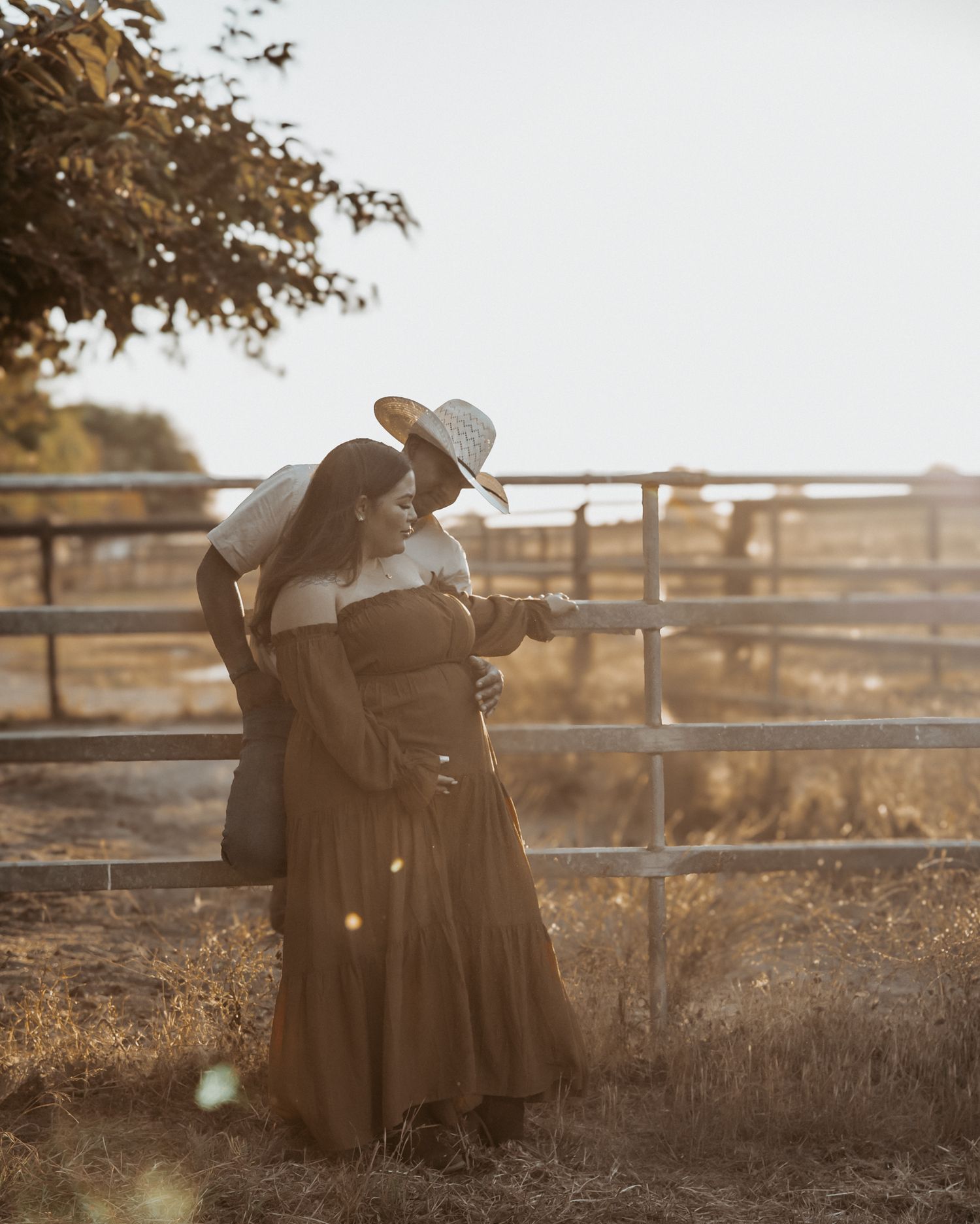Couple embracing near a rustic wooden fence at sunset creating a romantic silhouette against the golden sky.