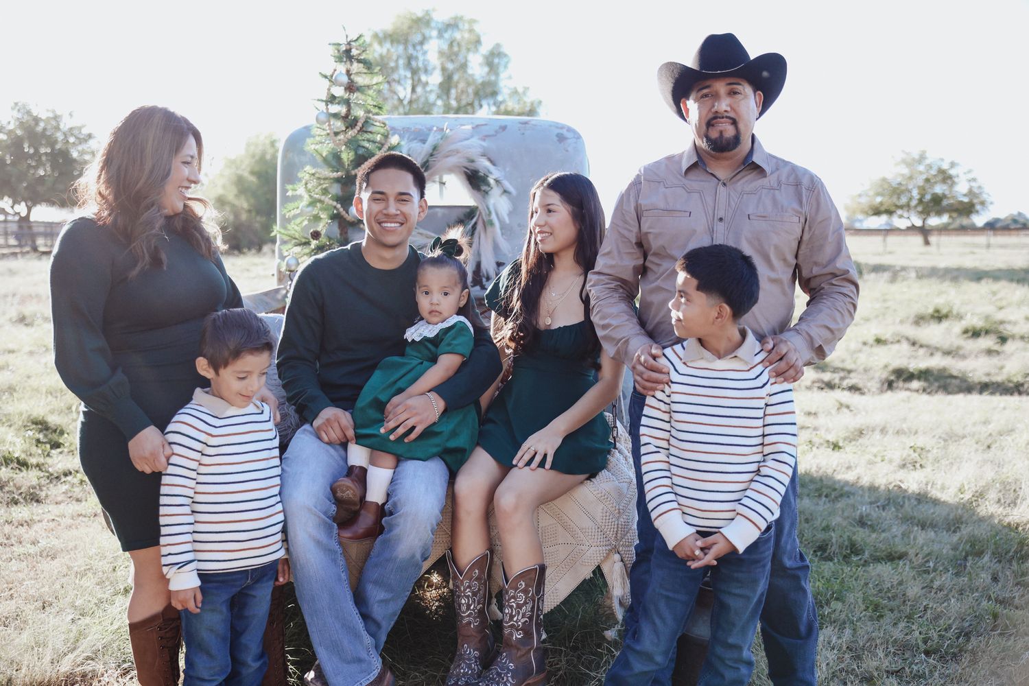 A group sits together outdoors in a rural setting with mountains and an RV visible in the background.