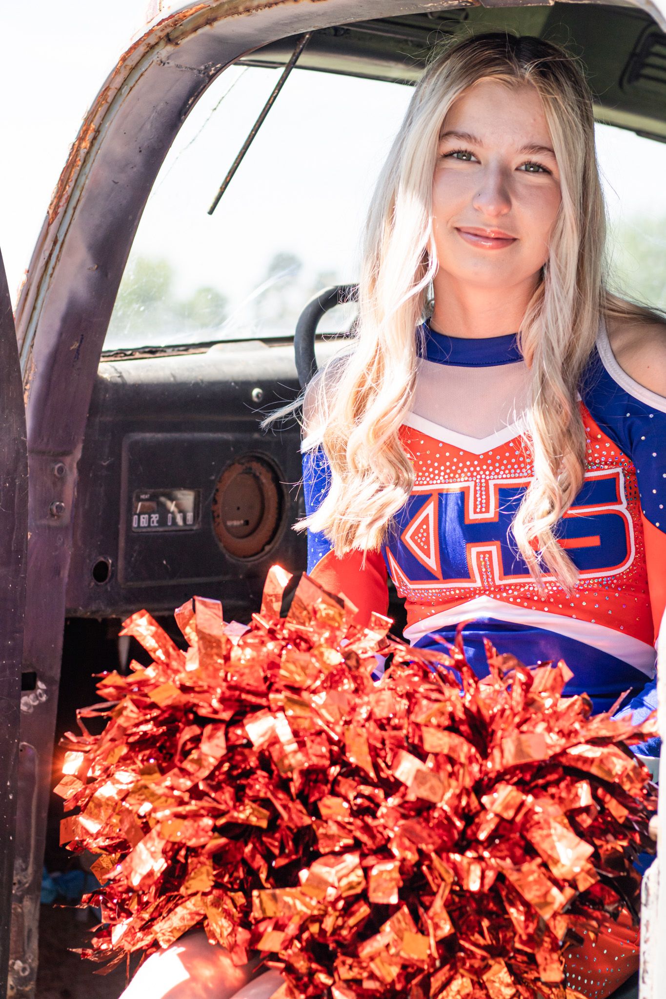 A cheerleader in blue uniform sits in a car holding bright orange pom poms in a photo series.
