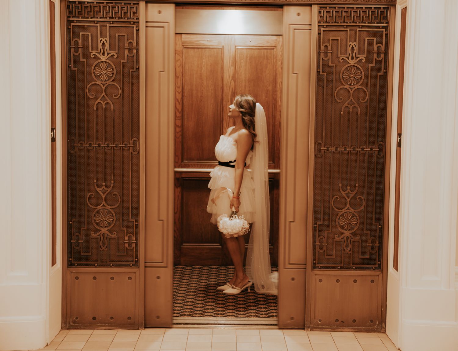 A vintage-style photograph of an elegant hallway with ornate wooden doors and decorative ironwork patterns.