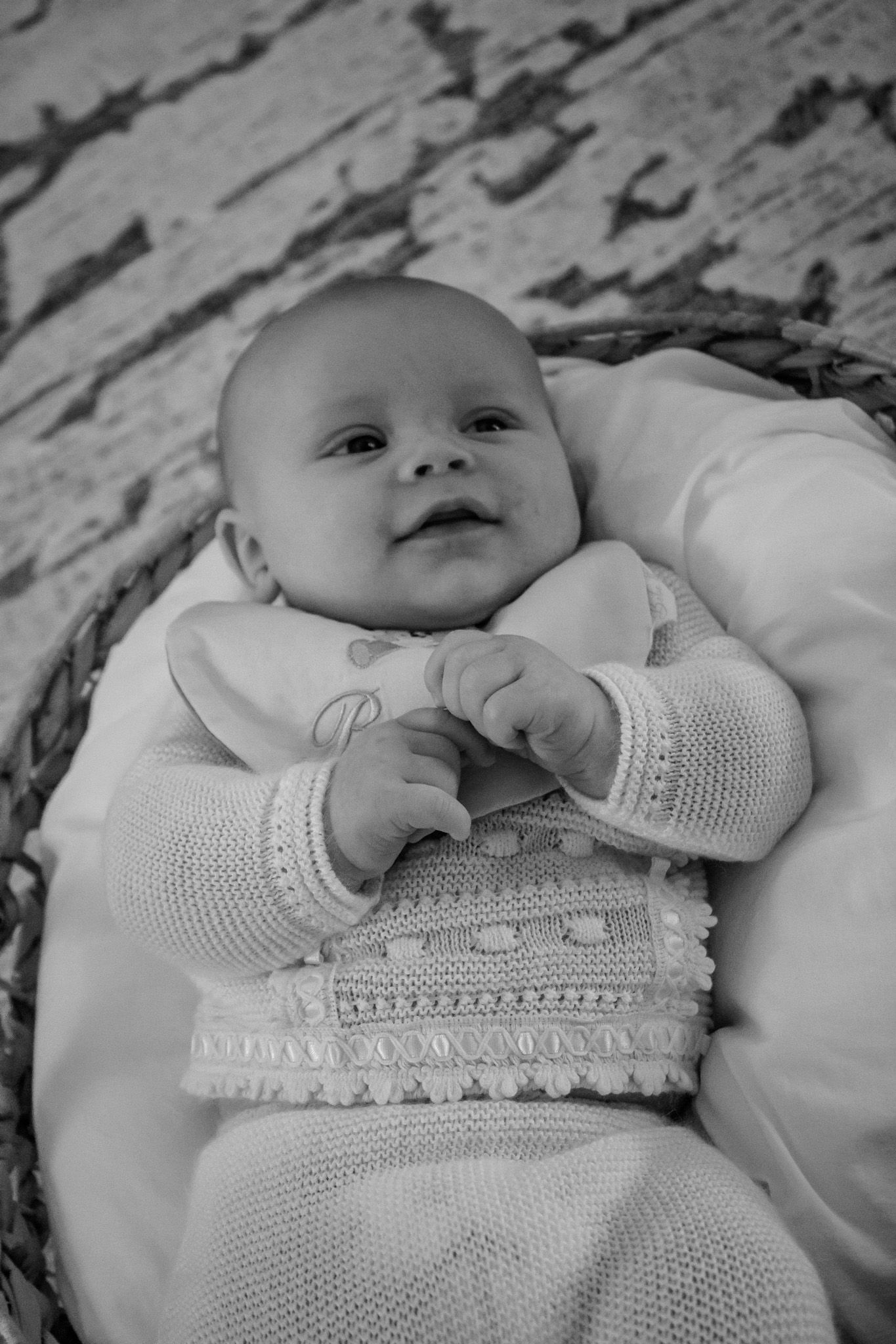 Black and white photo series showing a baby lying down in a delicate white knitted dress with lace details.