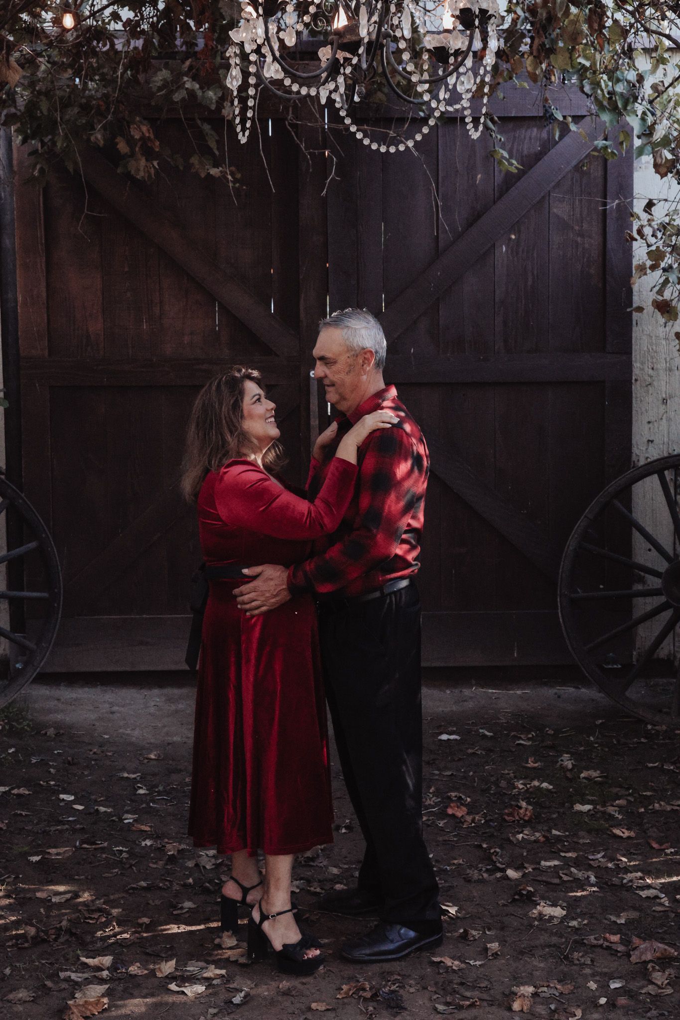 Romantic couple dancing together against a rustic barn backdrop with string lights and autumn leaves.