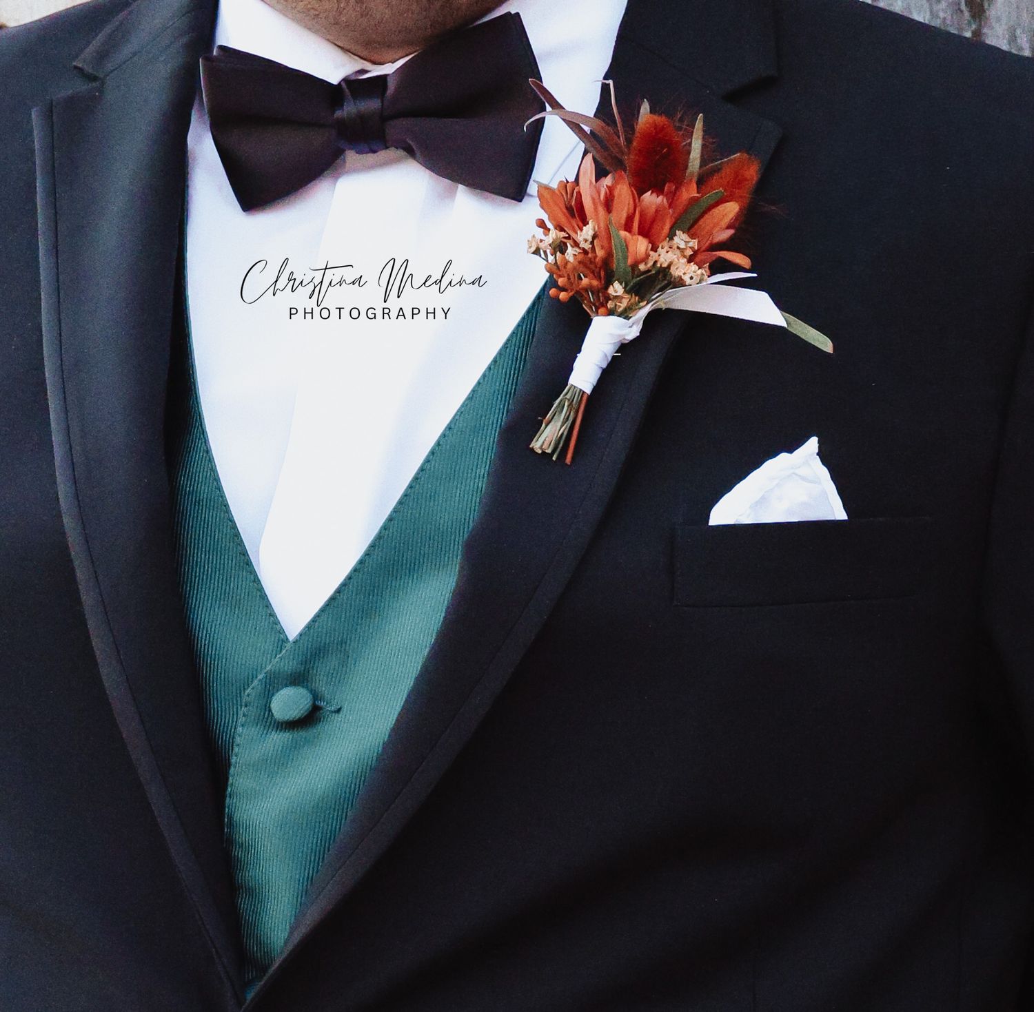 Close-up detail of a formal black tuxedo with emerald green vest and orange floral boutonniere.