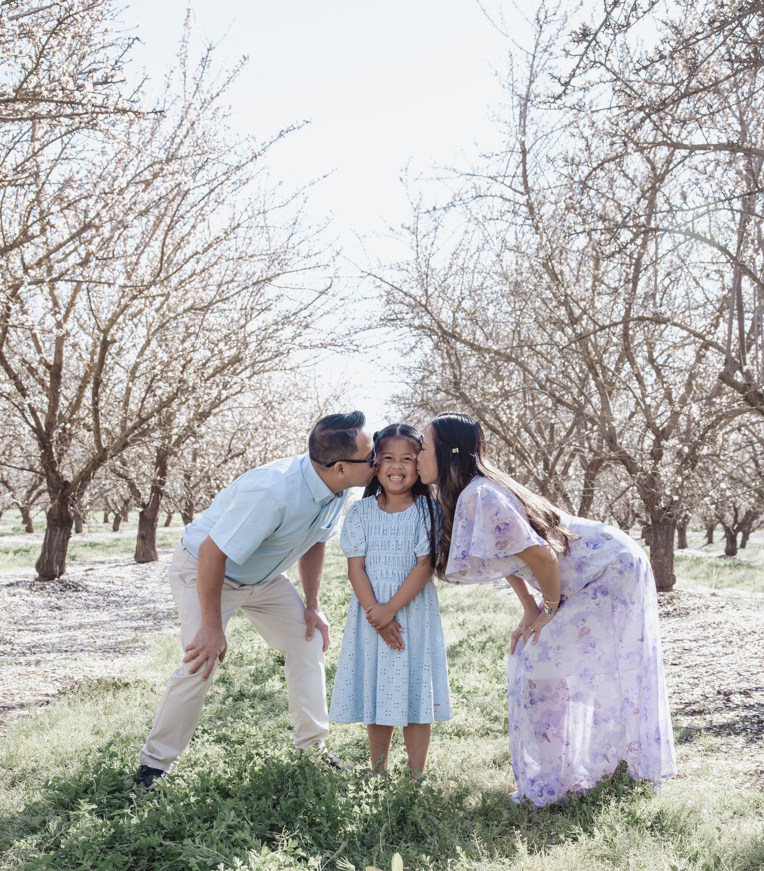 Family photo session in a blooming spring orchard with white blossoms.