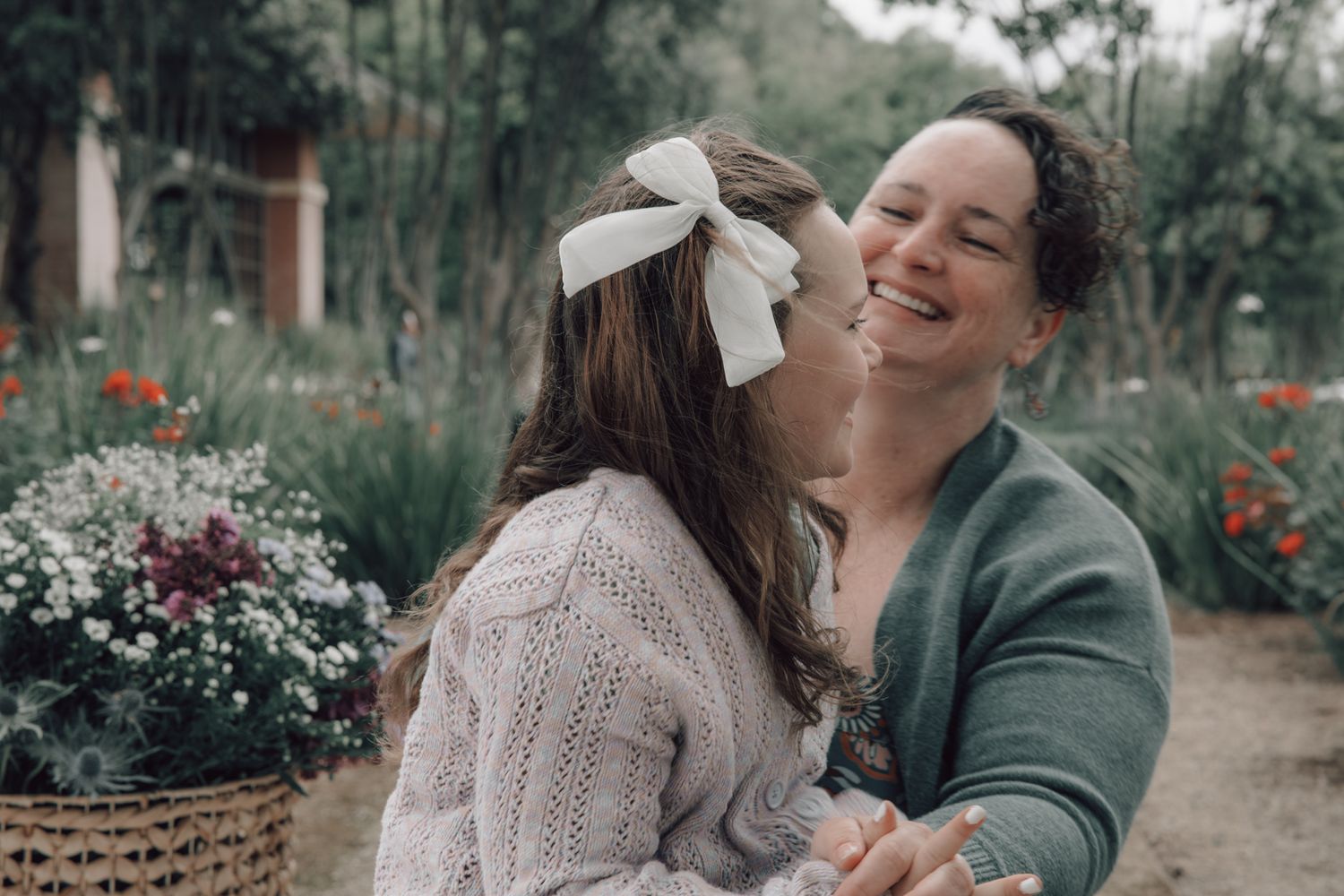 A tender moment shared between two people in a garden with soft lighting among blooming flowers and greenery.