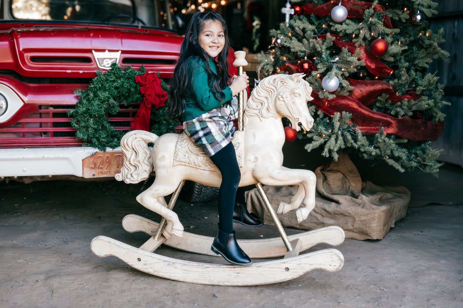 A wooden rocking horse with Christmas decorations and greenery in a festive holiday setting.