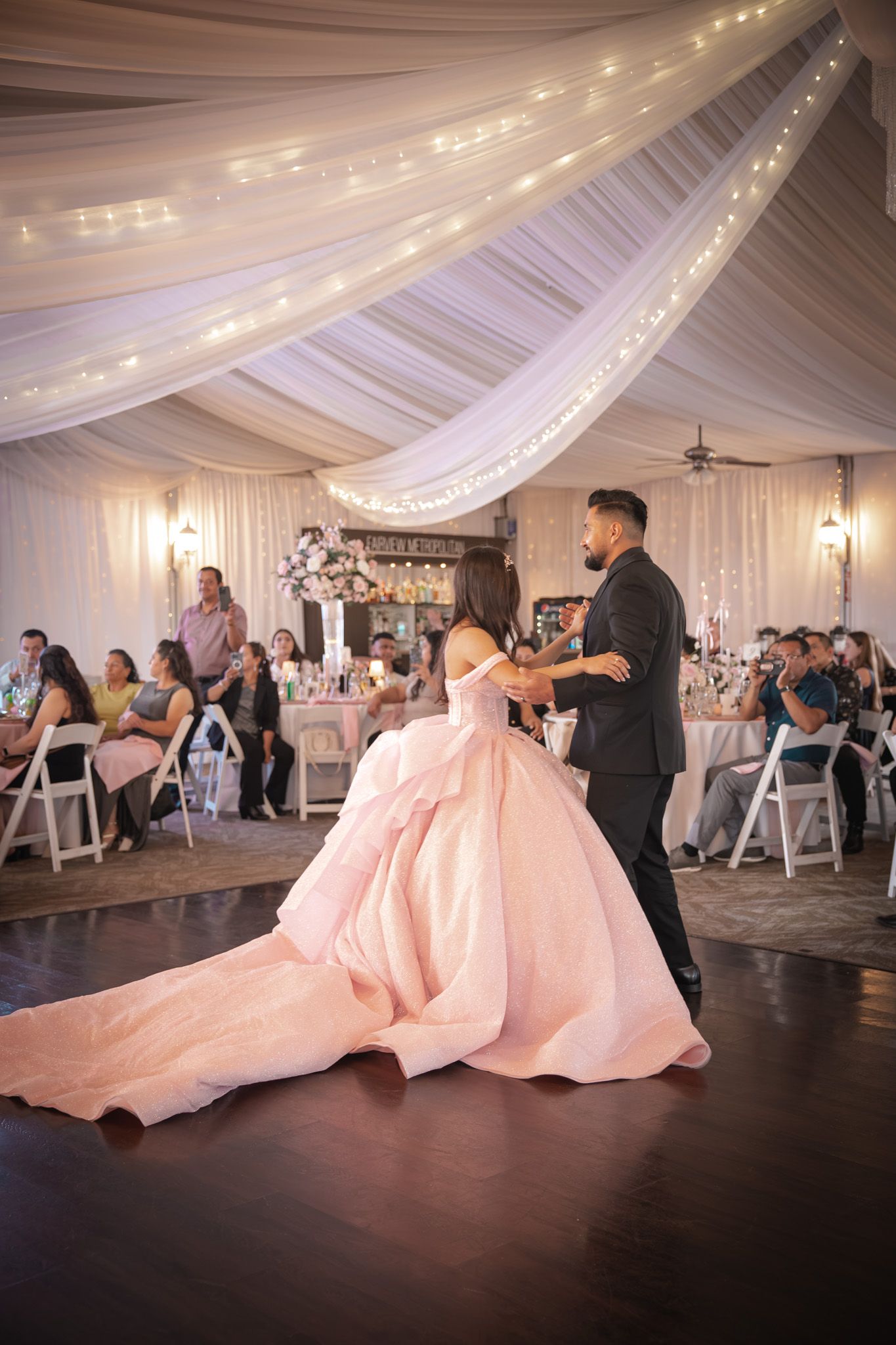 Candid quinceañera photo of the father and daughter embracing during their dance, warm lighting and emotional expressions.