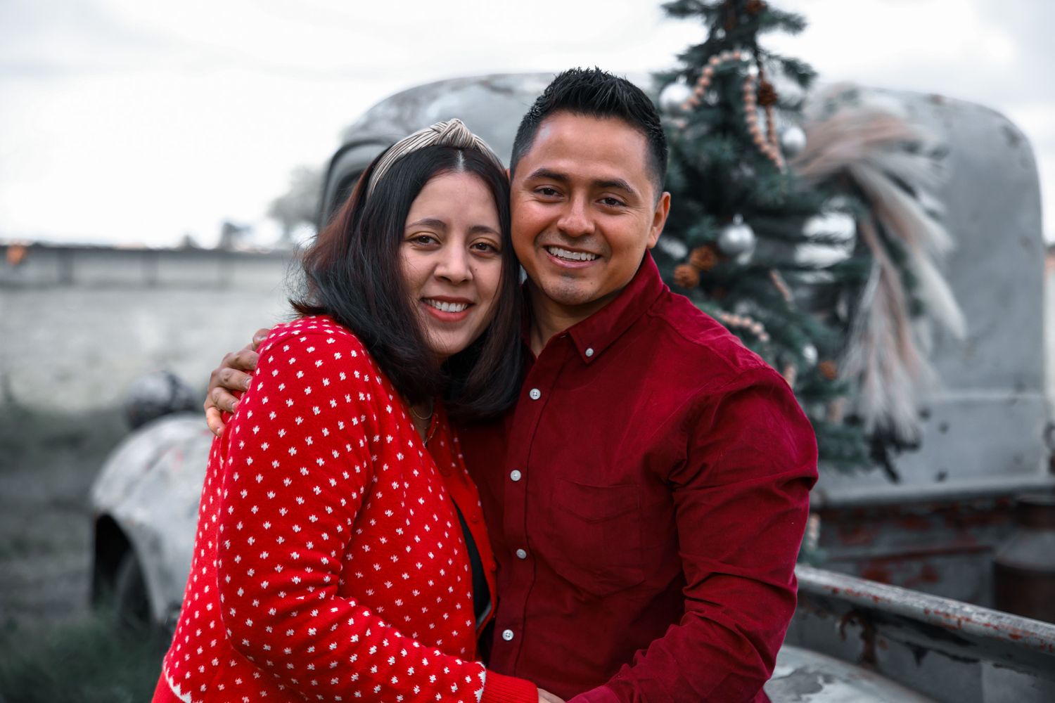 Couple in winter attire posing together outdoors with one person wearing a red polka dot dress.