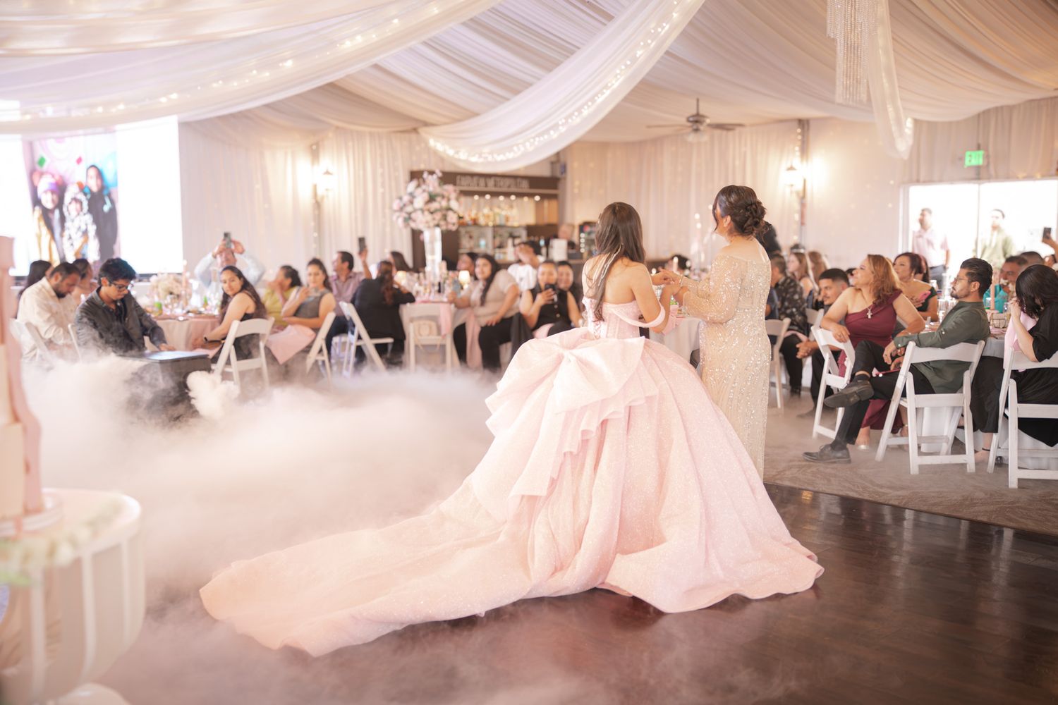 Candid quinceañera photo of the mother and daughter holding each other closely during their dance, emotional expressions and warm lighting.