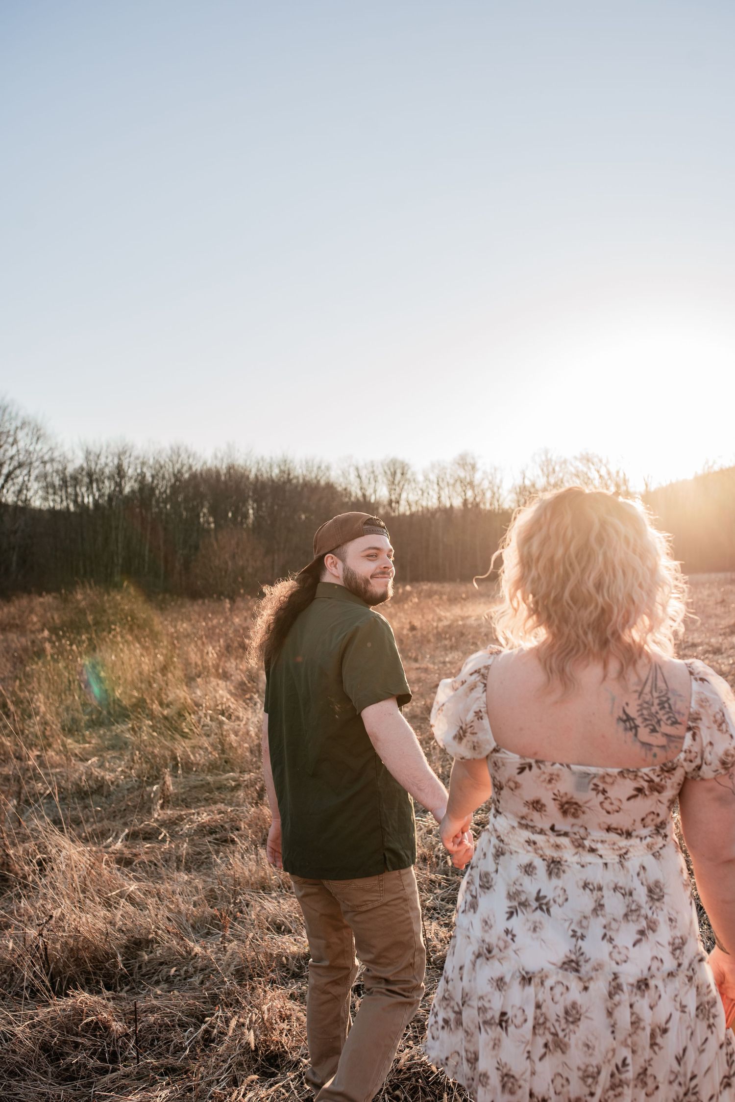 Man and woman walk hand in hand in field at golden hour. Couples' session in Schuylkill County