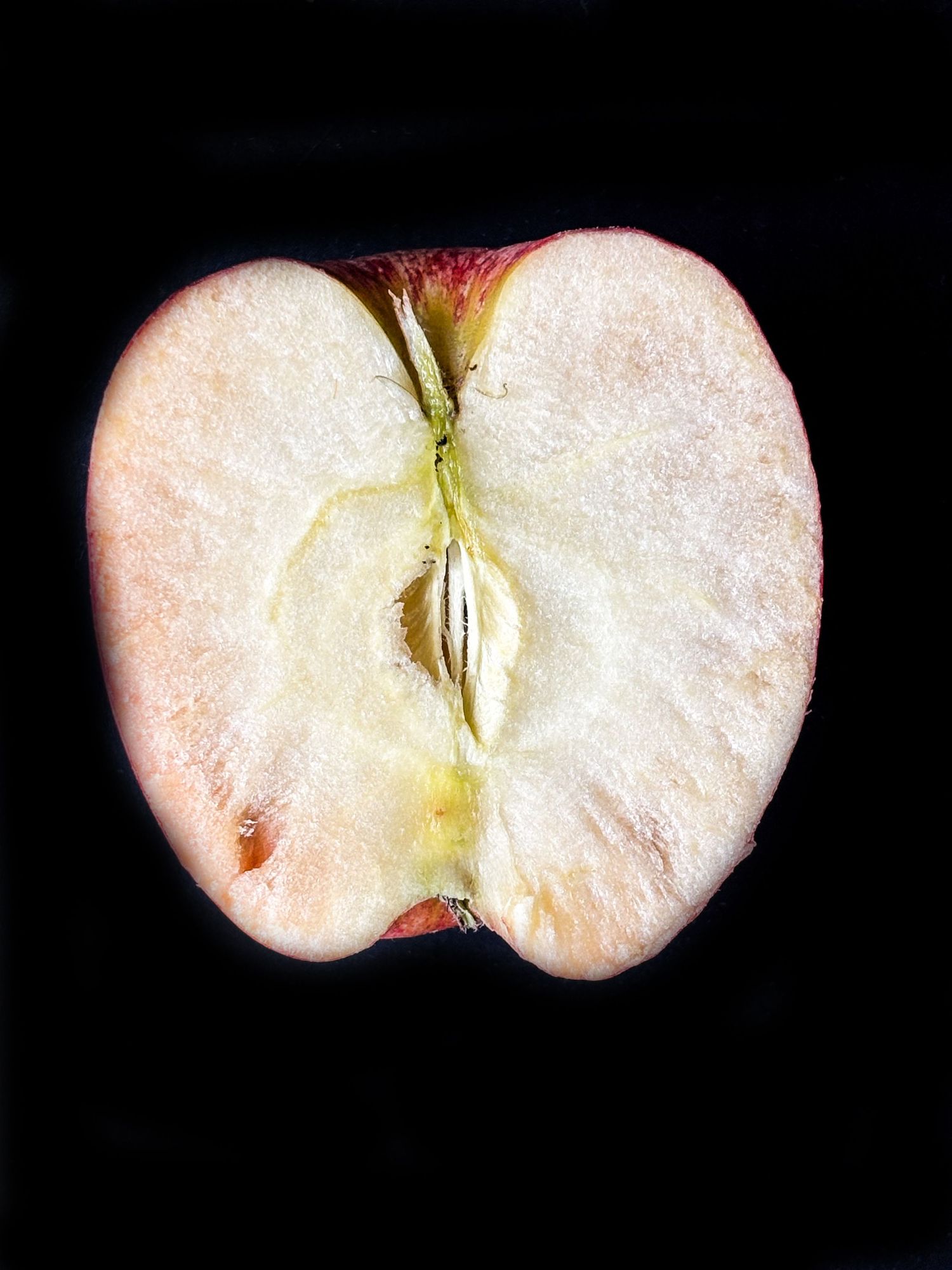 Cross-section of a fresh red apple cut in half, revealing white flesh and a single seed on black background.
