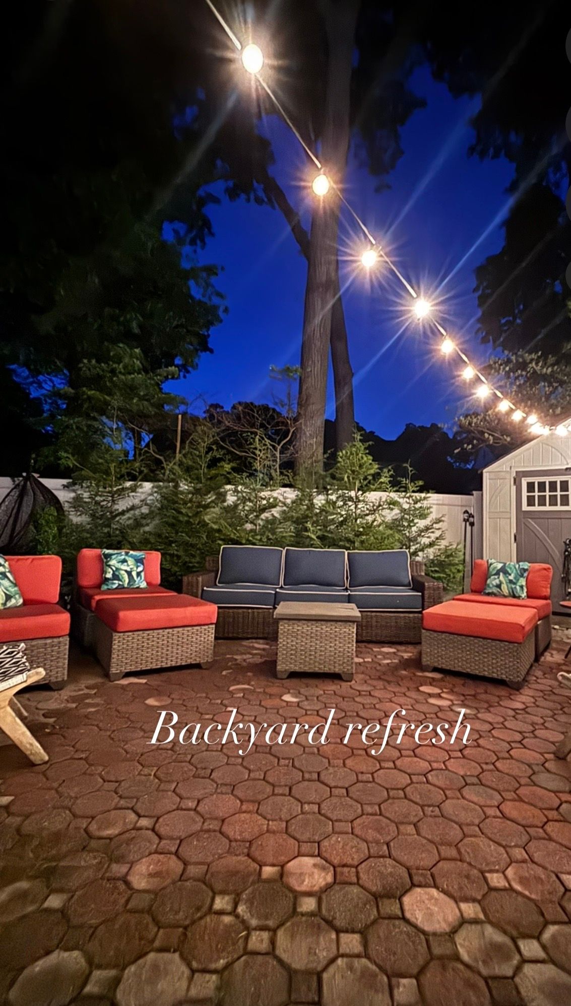 Cozy backyard patio at night with wicker furniture, red cushions, string lights, and brick pavers for an outdoor refresh.