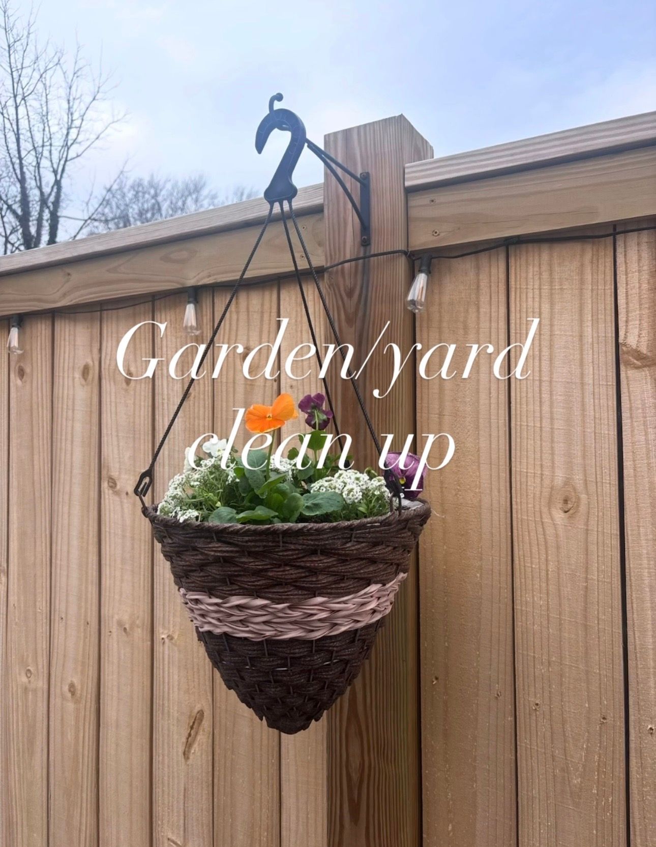 A wicker hanging basket with colorful flowers on a wooden fence, with text reading Garden/yard clean up.