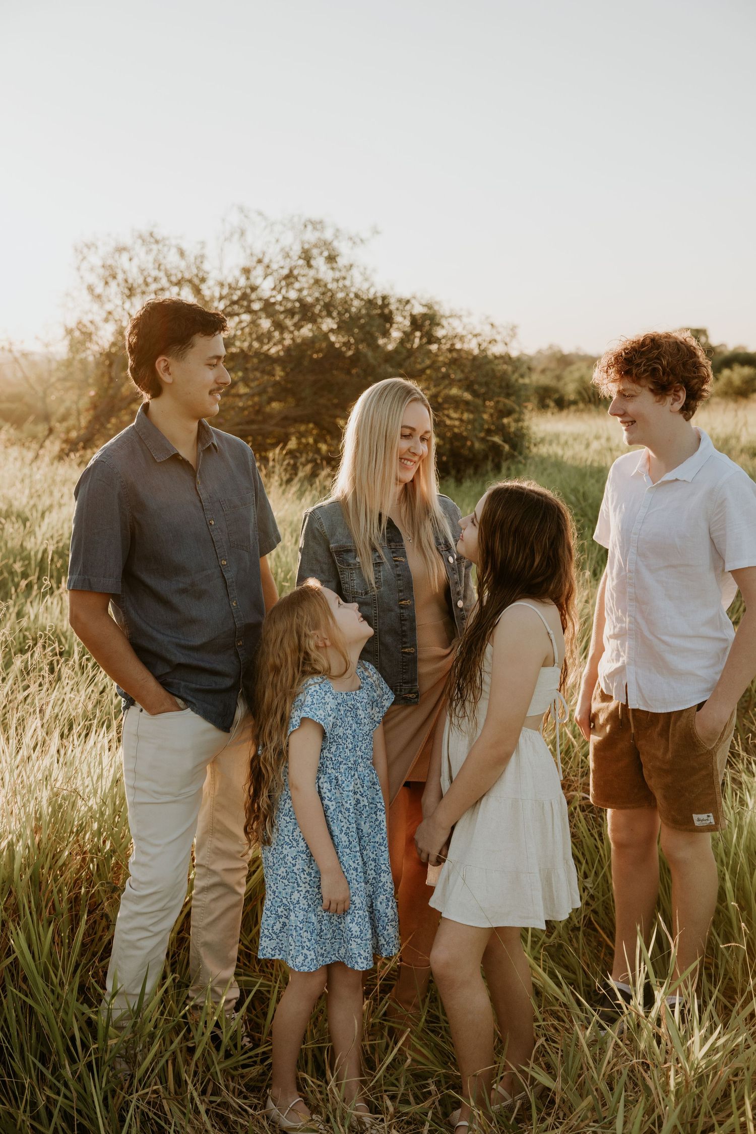 Family enjoying a sunset photoshoot in tall grass with warm golden lighting.