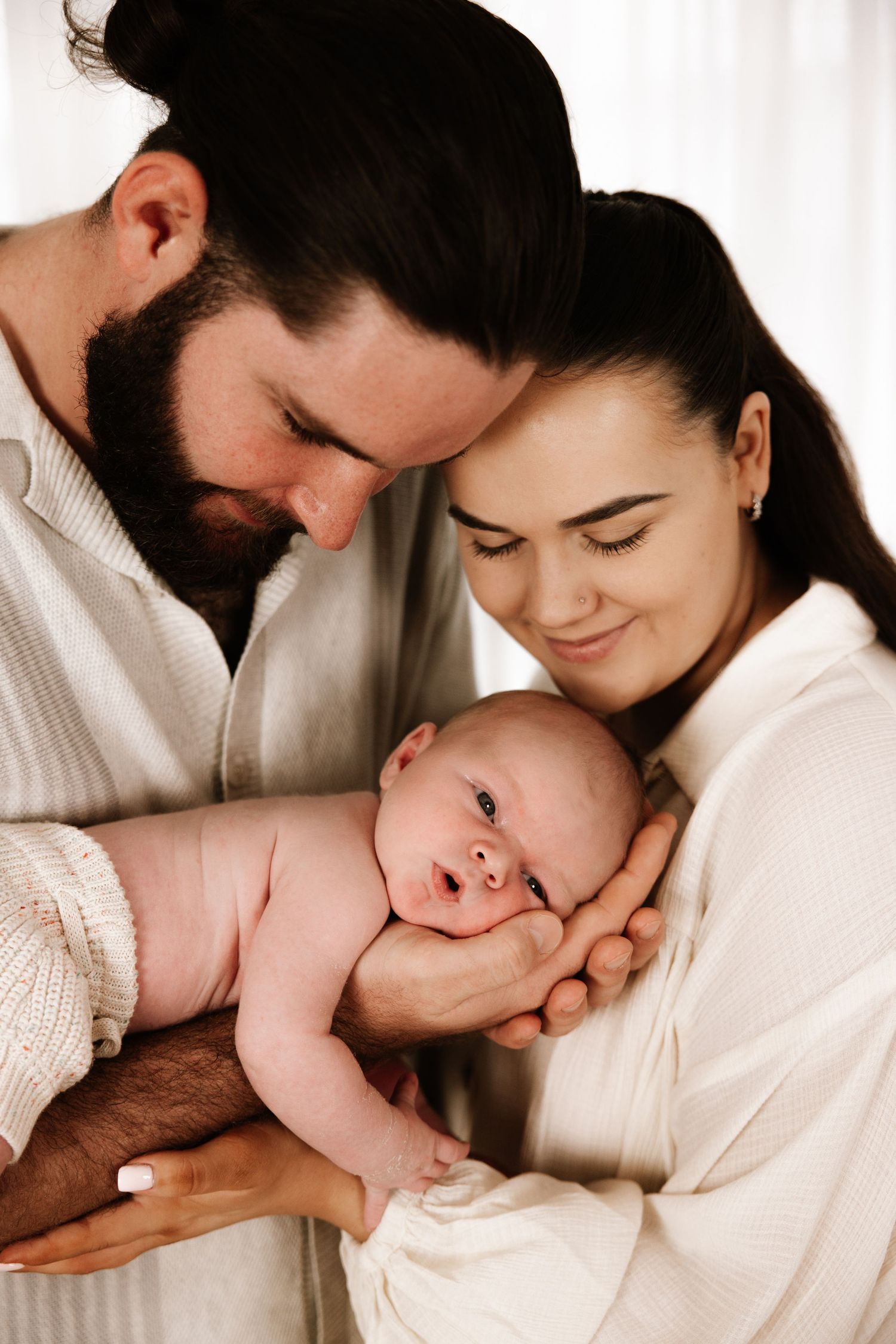 Intimate indoor family portrait with newborn in soft natural light.