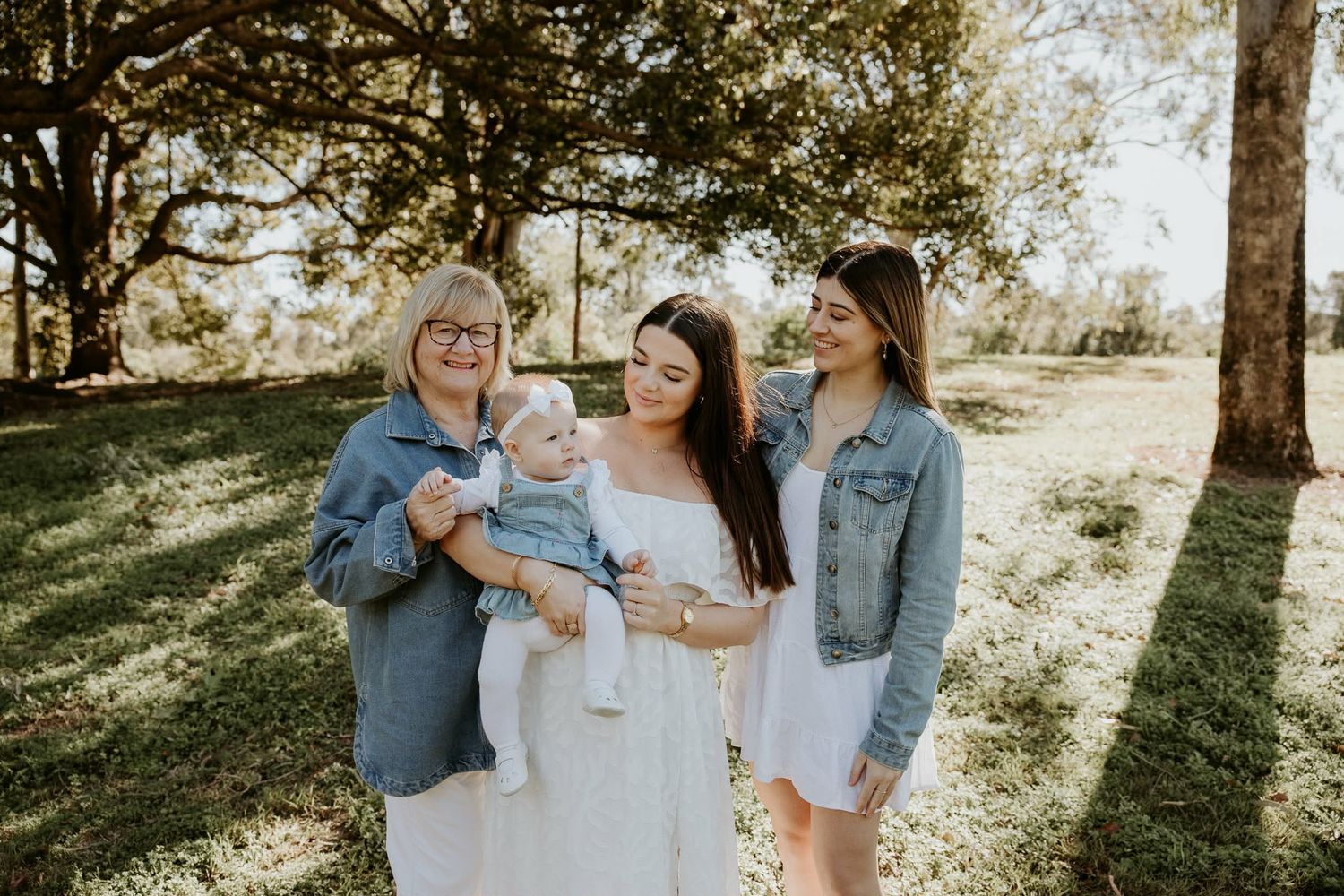 A casual outdoor family photoshoot with denim and white clothing under trees.
