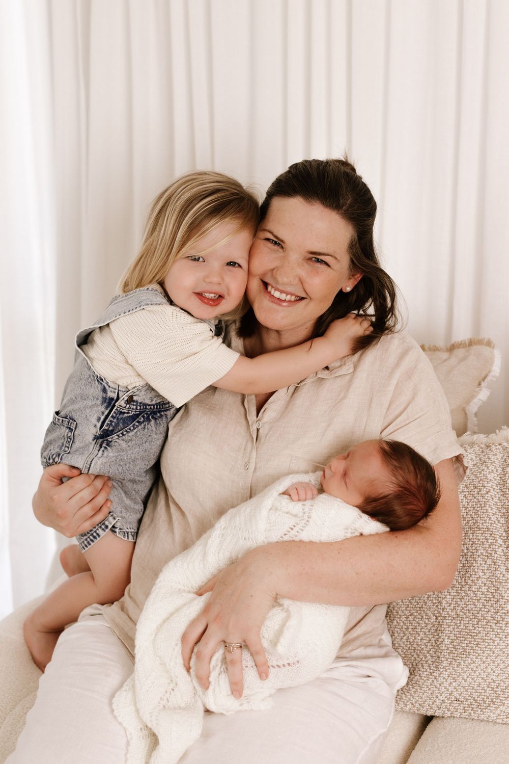 Indoor family portrait series showing tender moments with newborn baby on white couch.