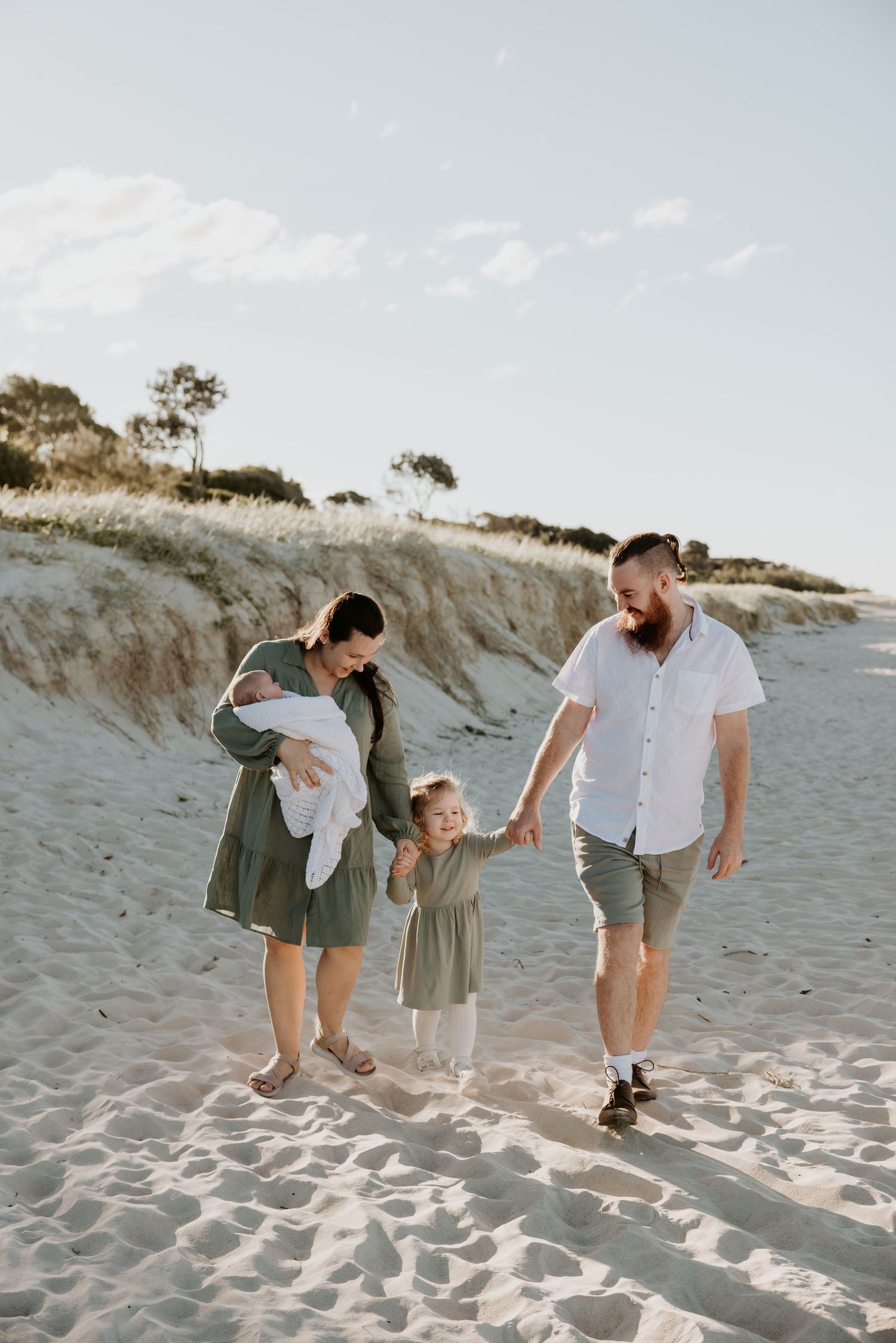 Family playing and walking together on sandy beach dunes during photo session.