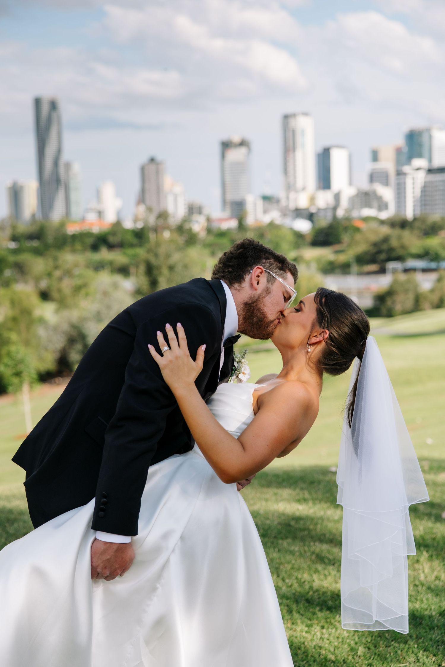 Romantic wedding kiss with city skyline backdrop in background.