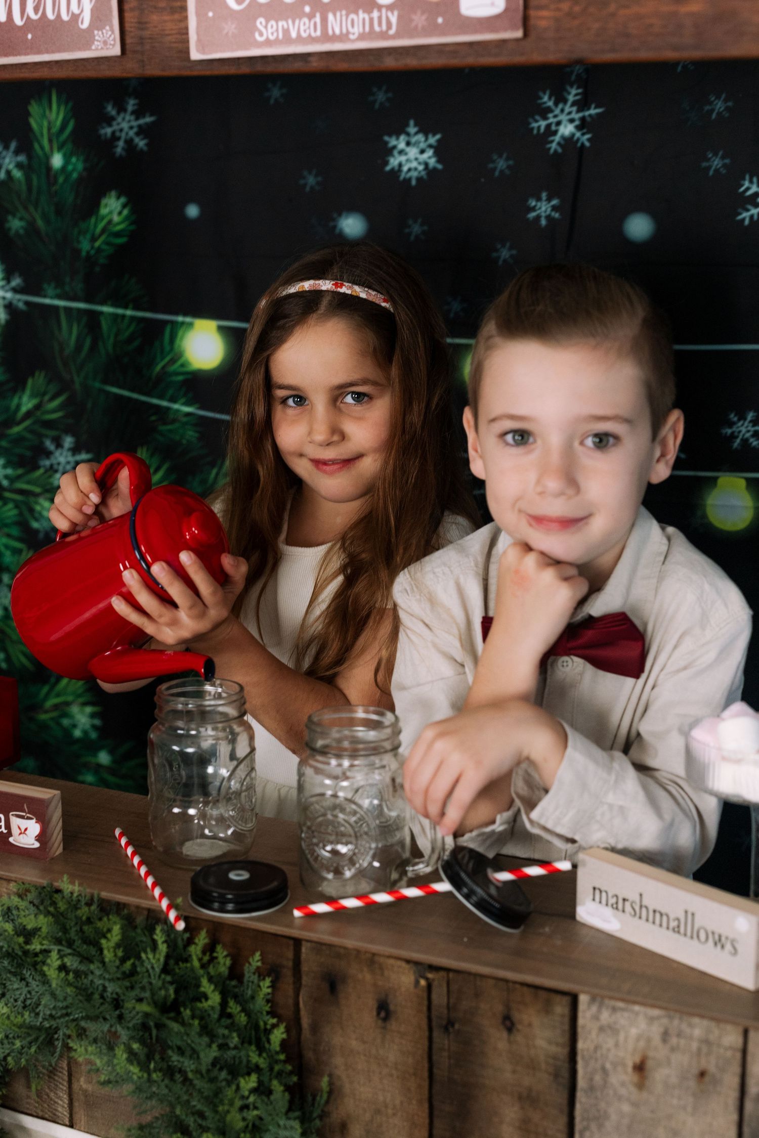 Children pose with mason jars and marshmallows at festive holiday photo booth.