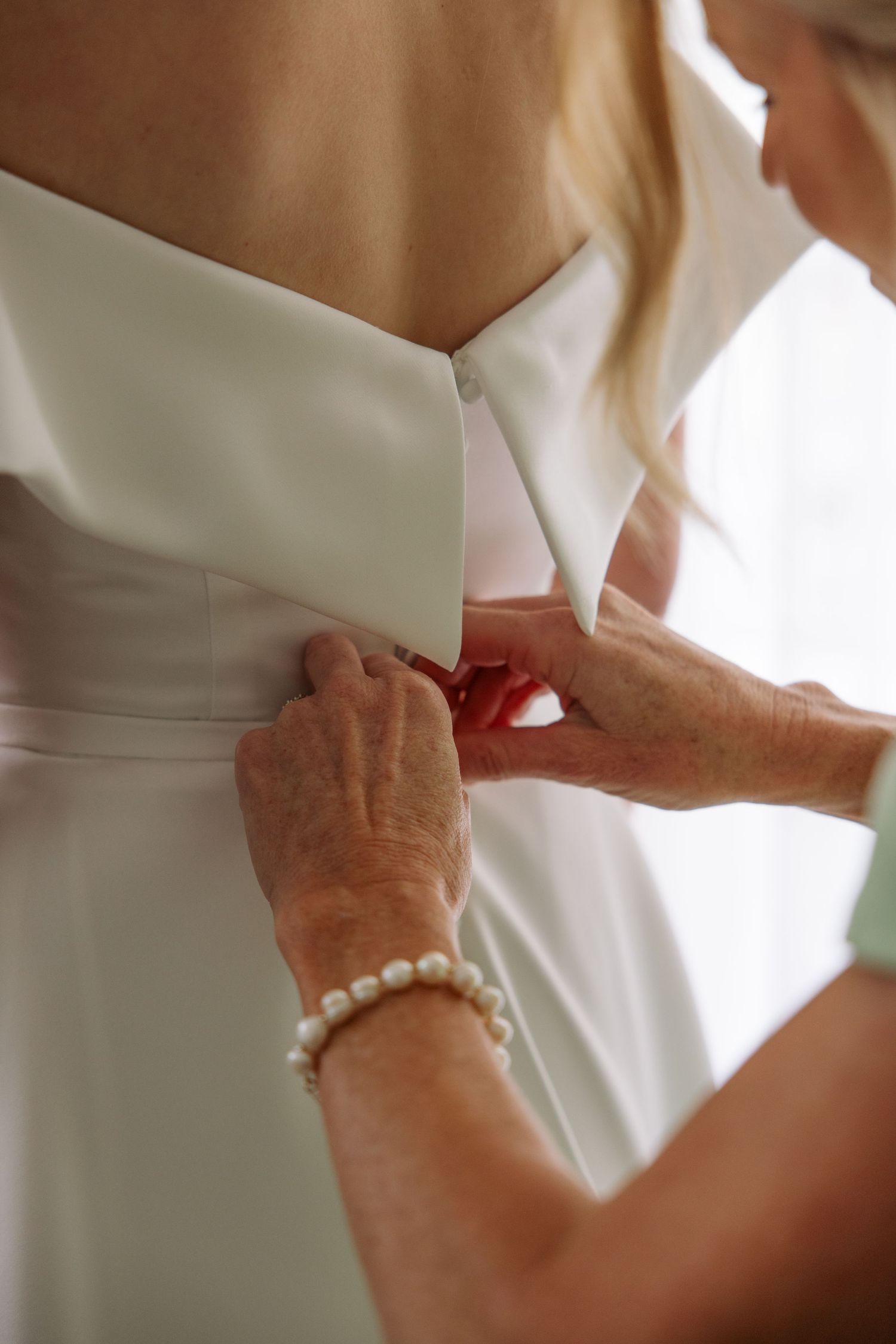 Close-up detail shot of pearl bracelet and wedding dress being fastened.