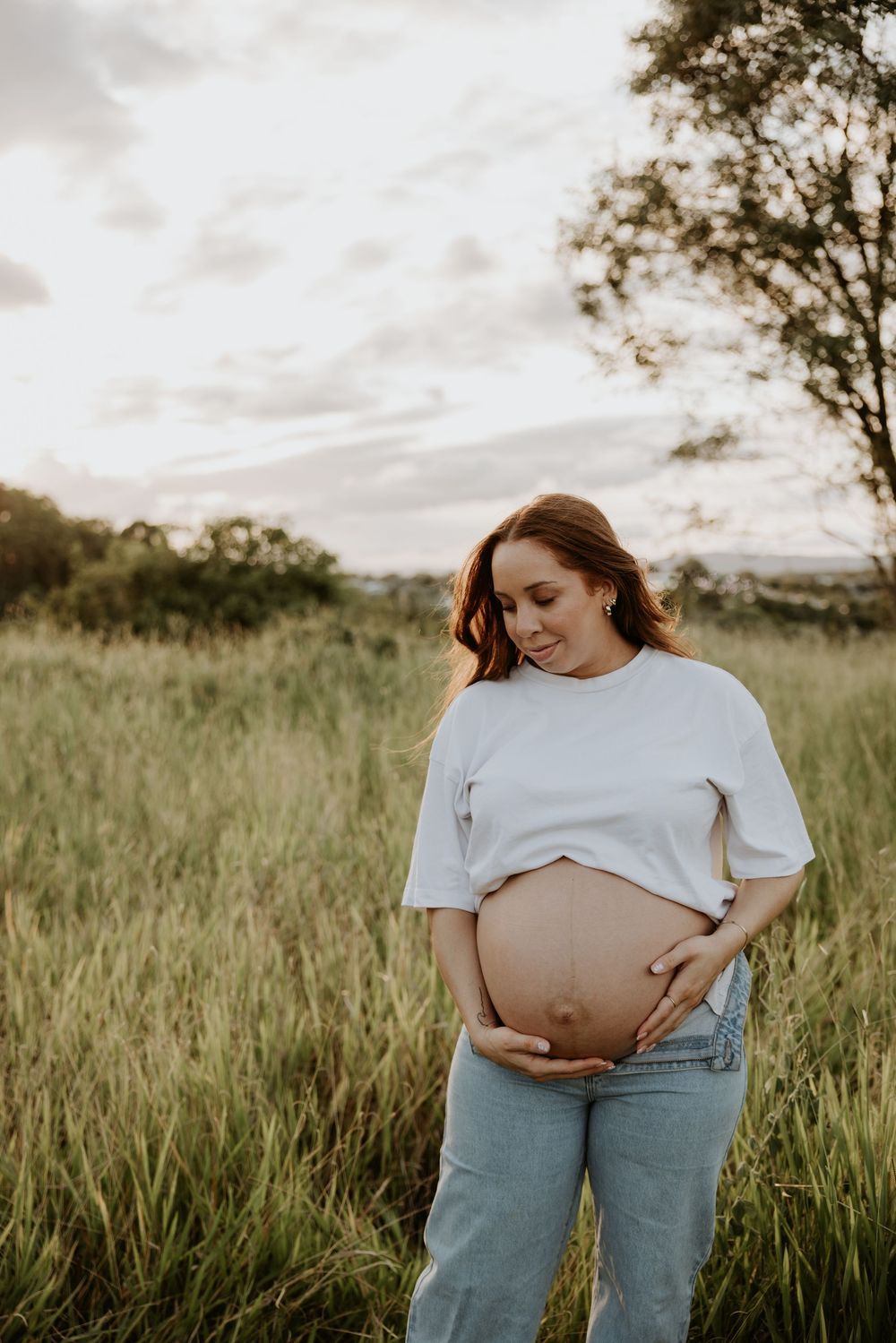 Maternity photo shoot in tall grass field during golden hour.