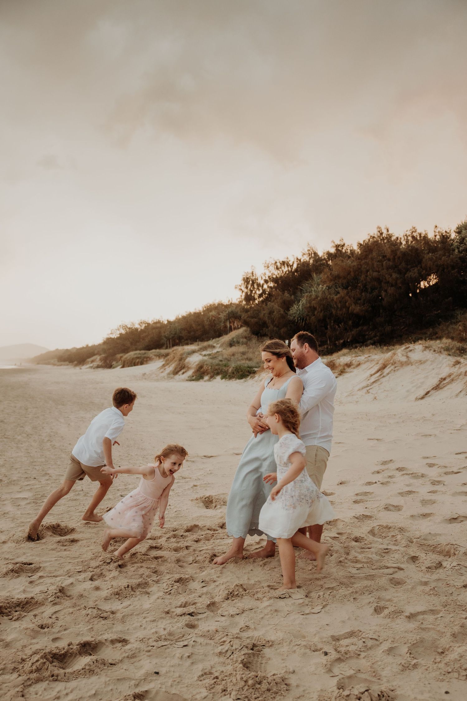 Family playing and running together on sandy beach dunes at sunset.