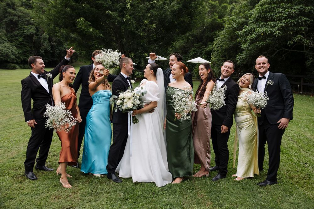 Wedding party gathered outdoors for group photos on a lush green lawn.