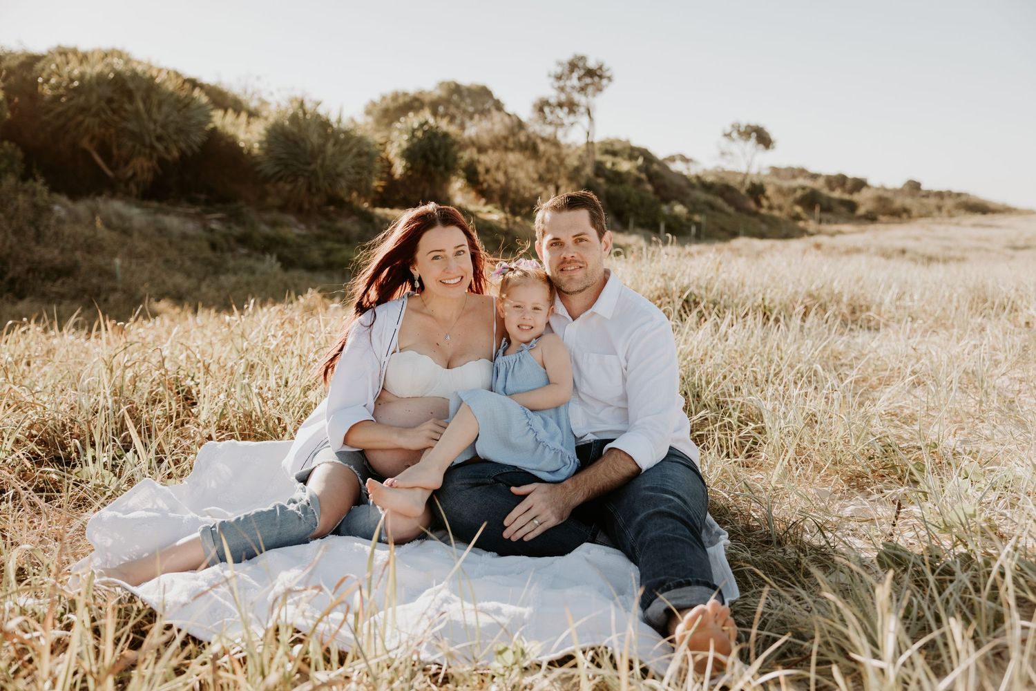 Family relaxing together on grassy hillside during golden hour.