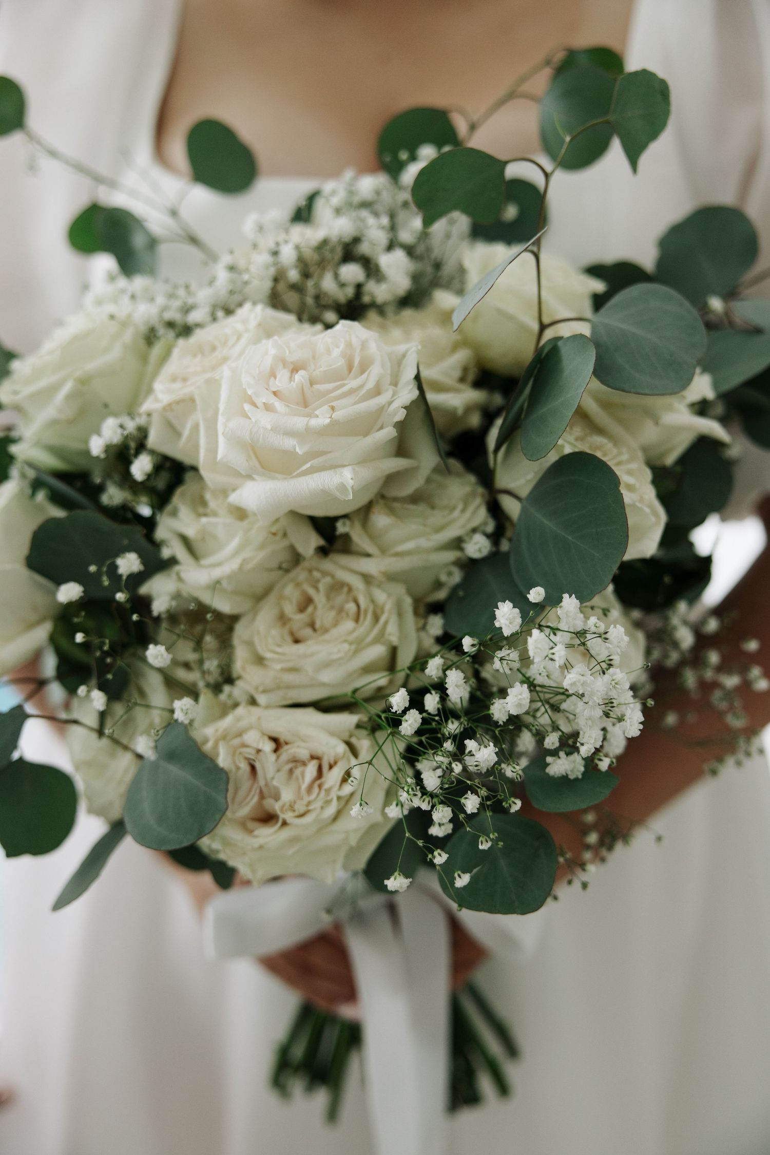Elegant white rose and eucalyptus wedding bouquet with baby's breath accents.