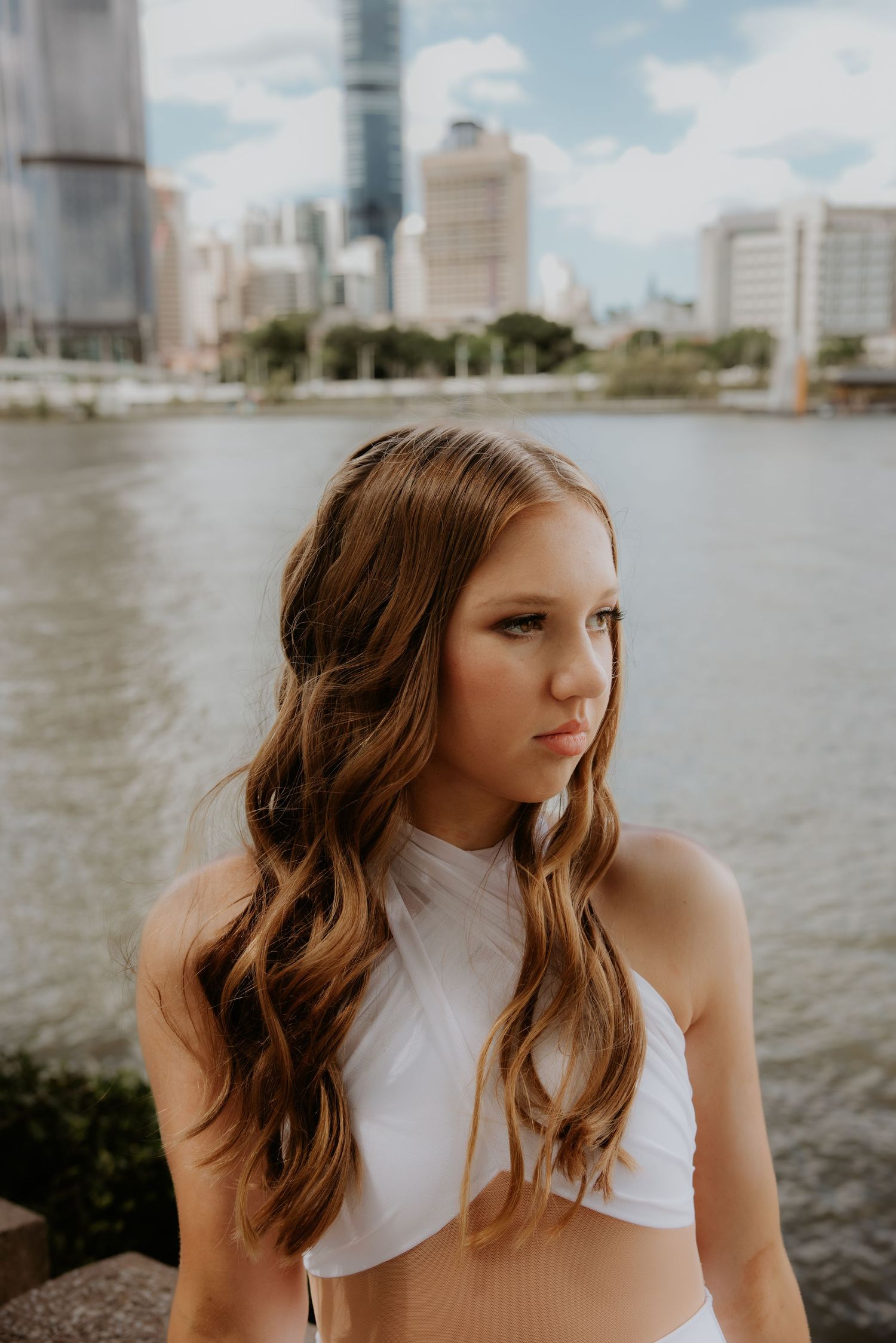 Portrait by the riverside with city skyline and buildings in background.