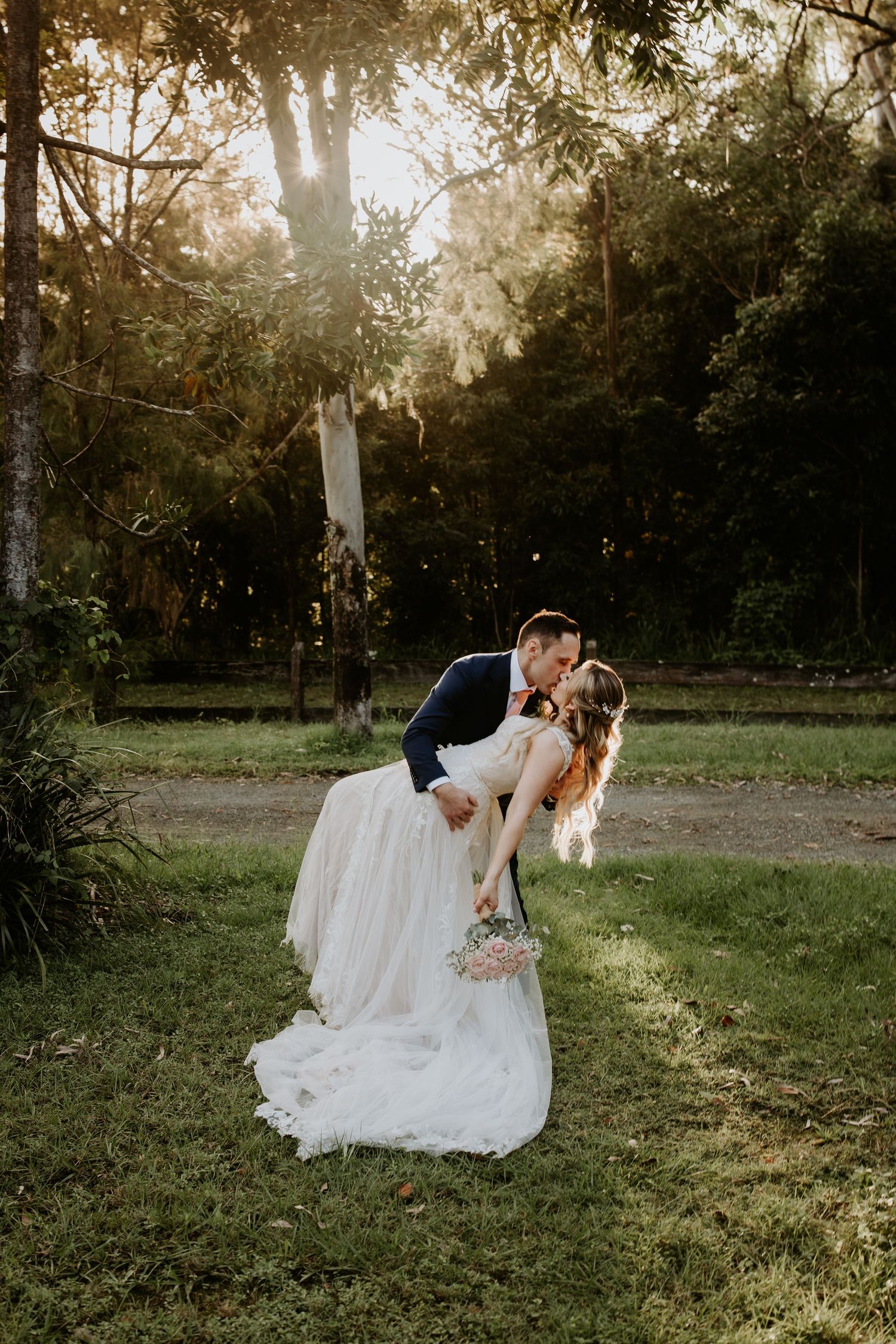 A romantic sunset wedding photo session in a grassy field with golden light filtering through trees.