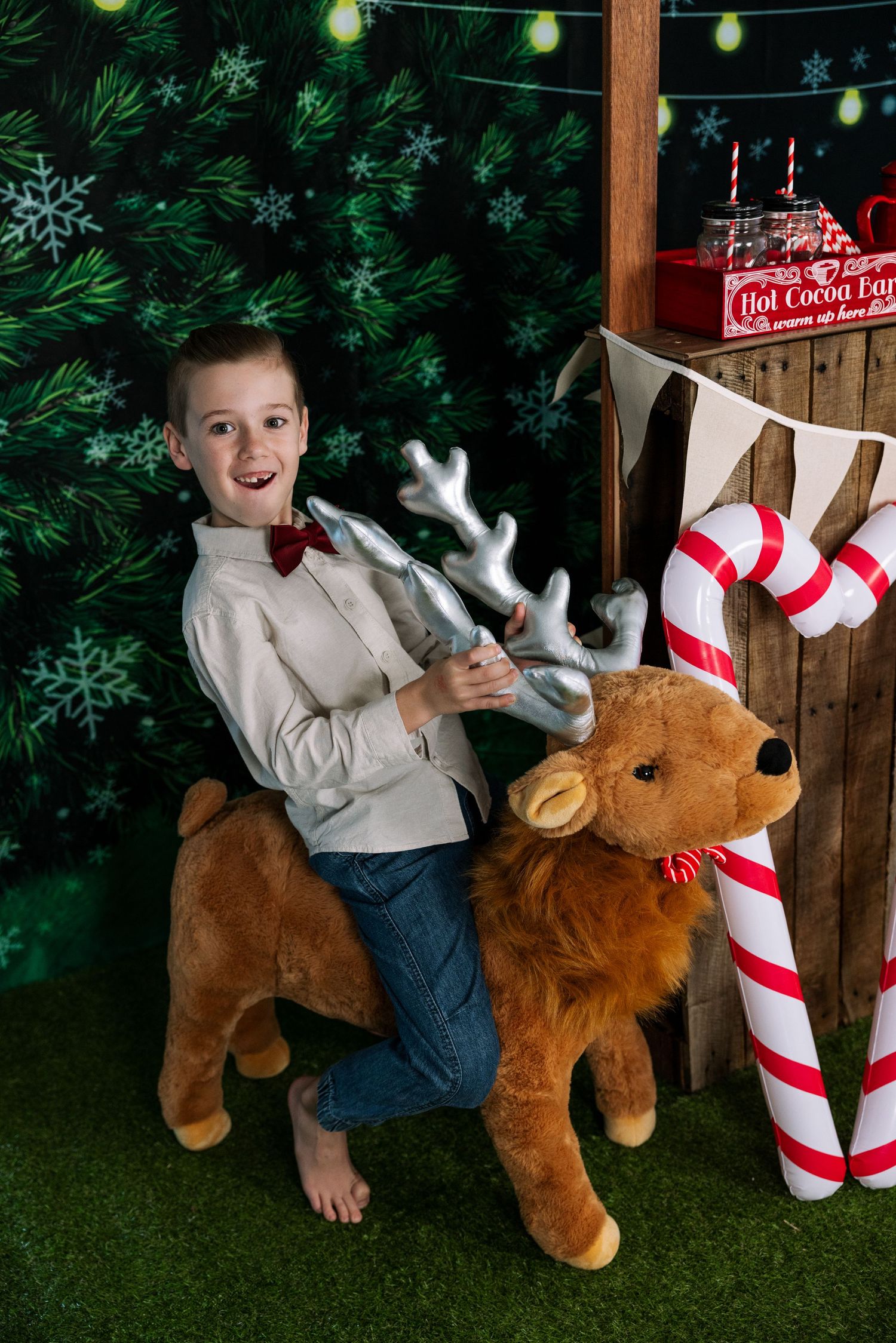 Child plays with stuffed reindeer and candy cane props at Christmas-themed photo booth.