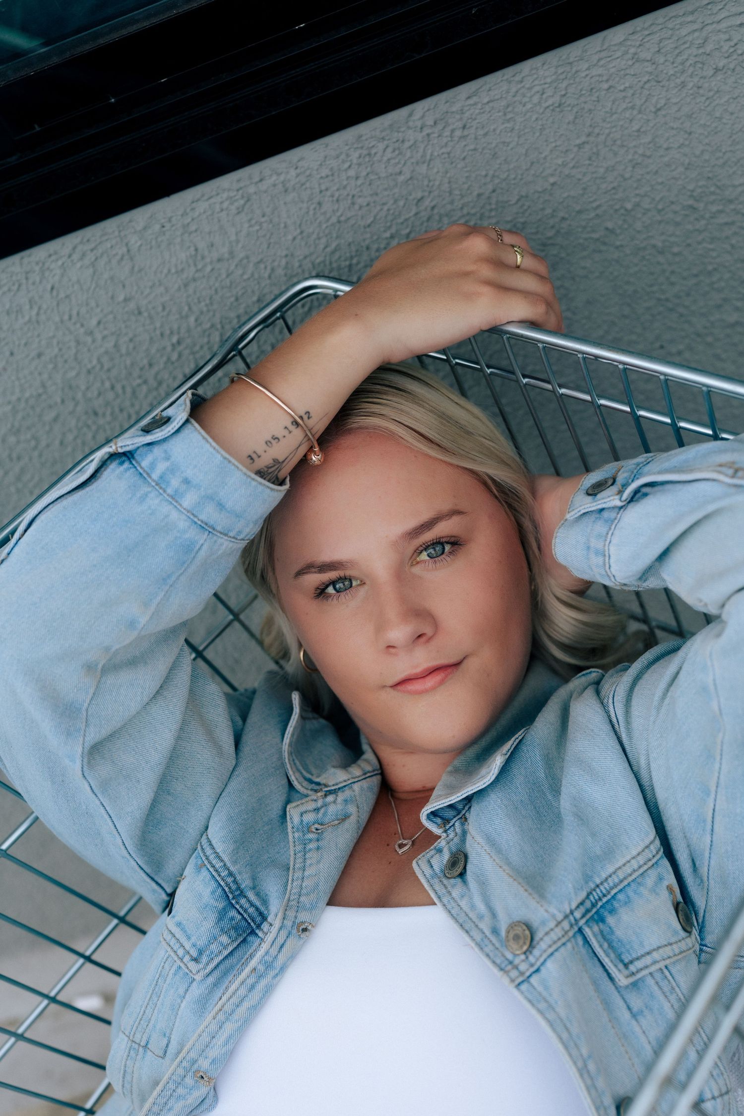 A casual portrait of someone lying in a shopping cart wearing a light denim jacket.