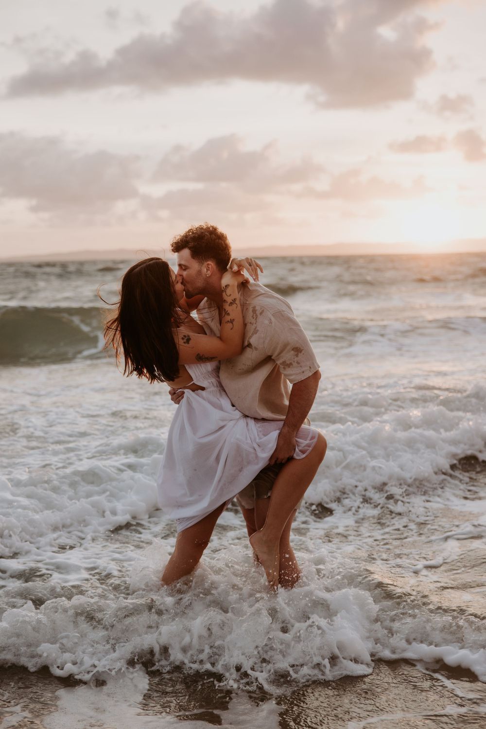 Romantic couple playing in ocean waves at sunset on a beach.