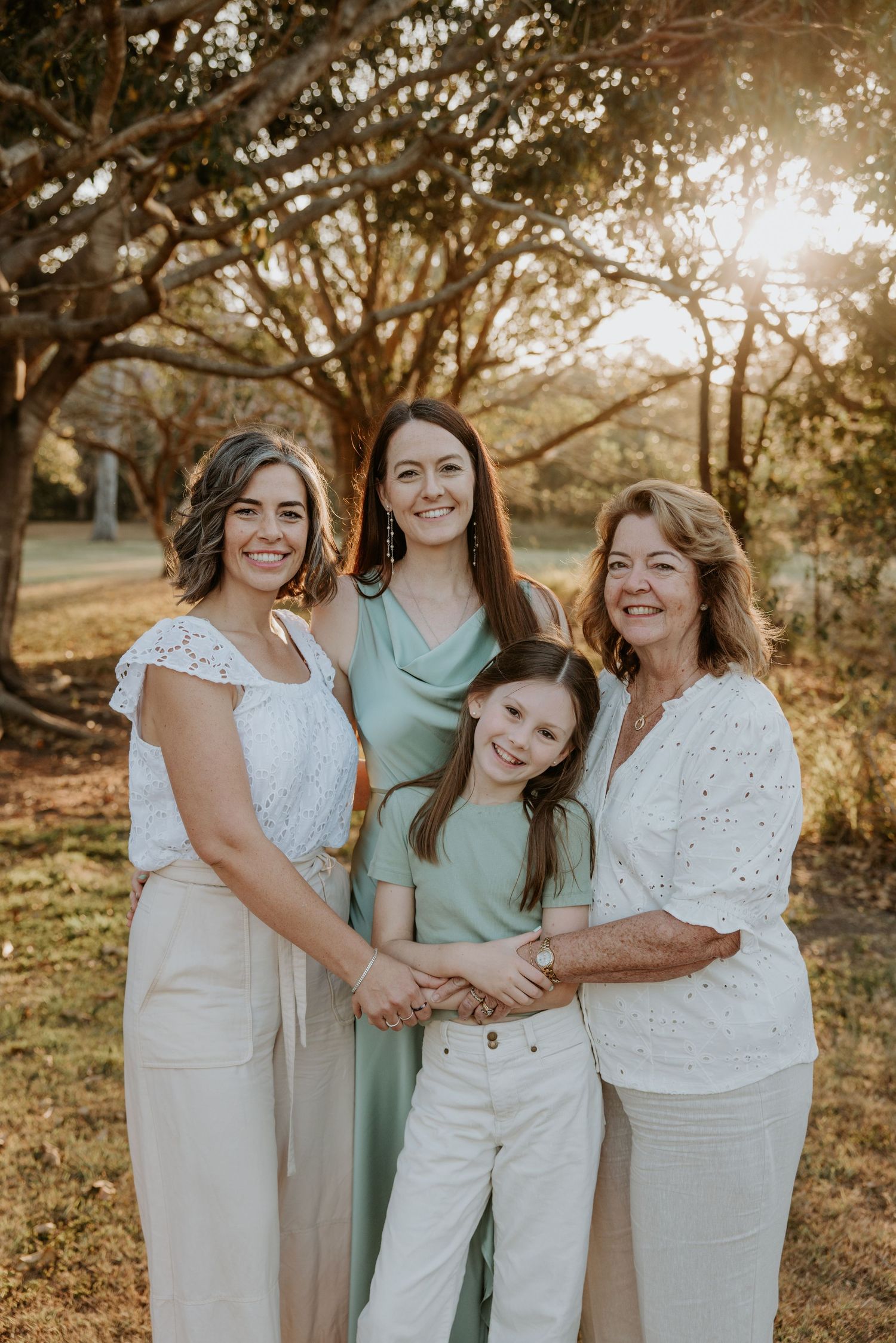 Group of women in coordinated white and mint outfits pose together in warm sunset lighting.