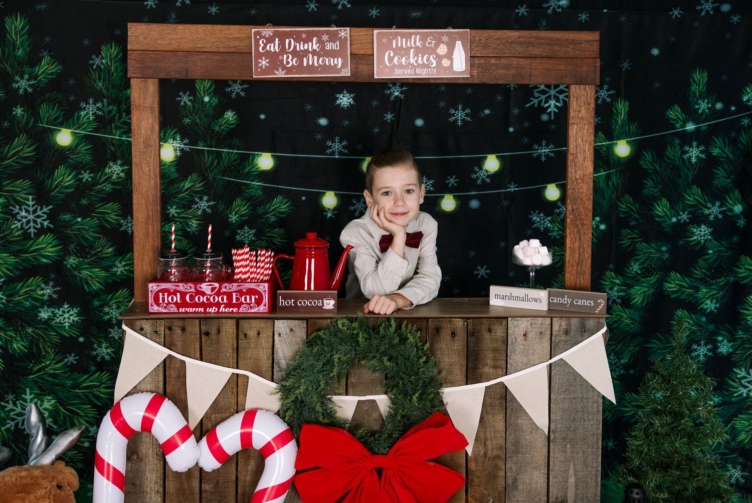 Holiday photo booth setup with wooden signs, string lights, and festive Christmas decorations.